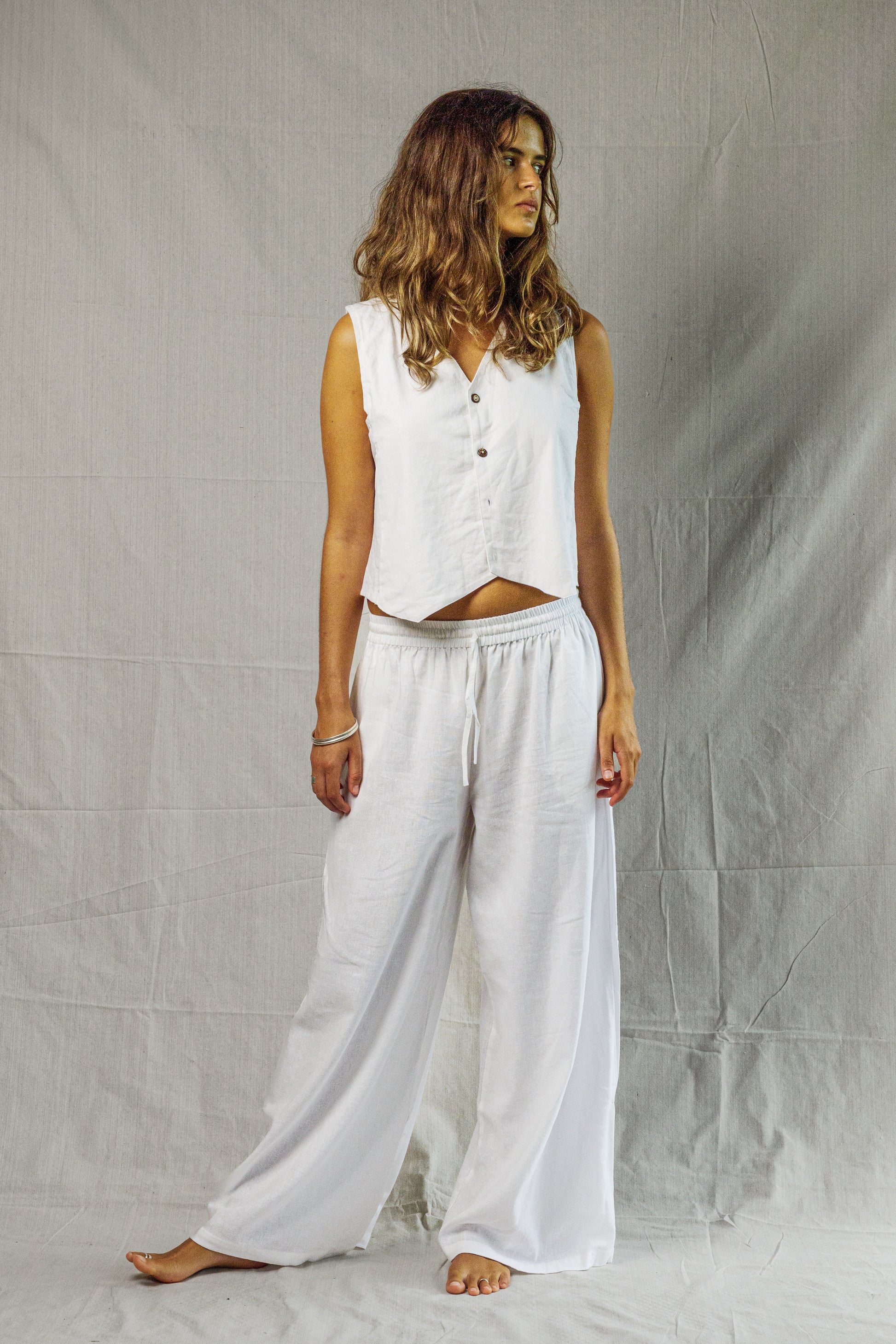 White sleeveless linen vest with buttons and a relaxed fit on model.