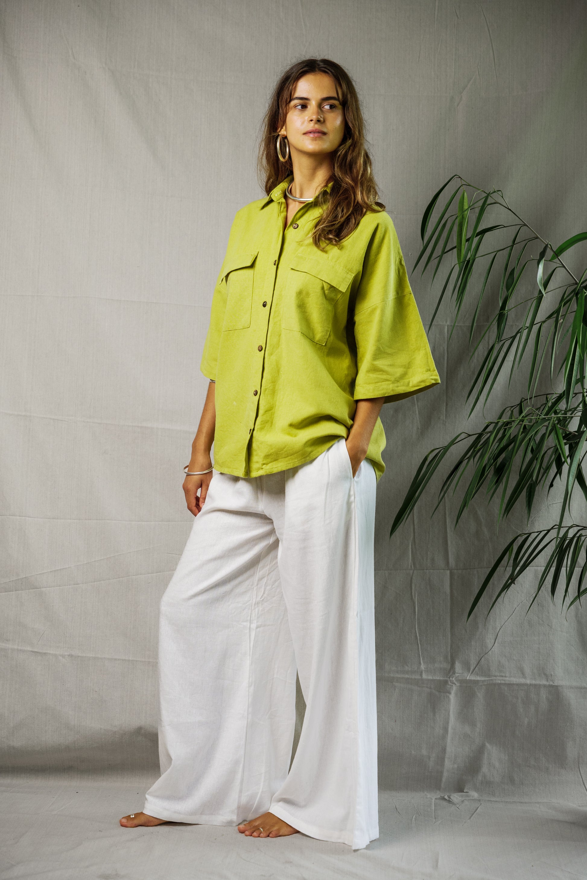 Lime green oversized linen shirt with short sleeves worn with wide-leg white pants.