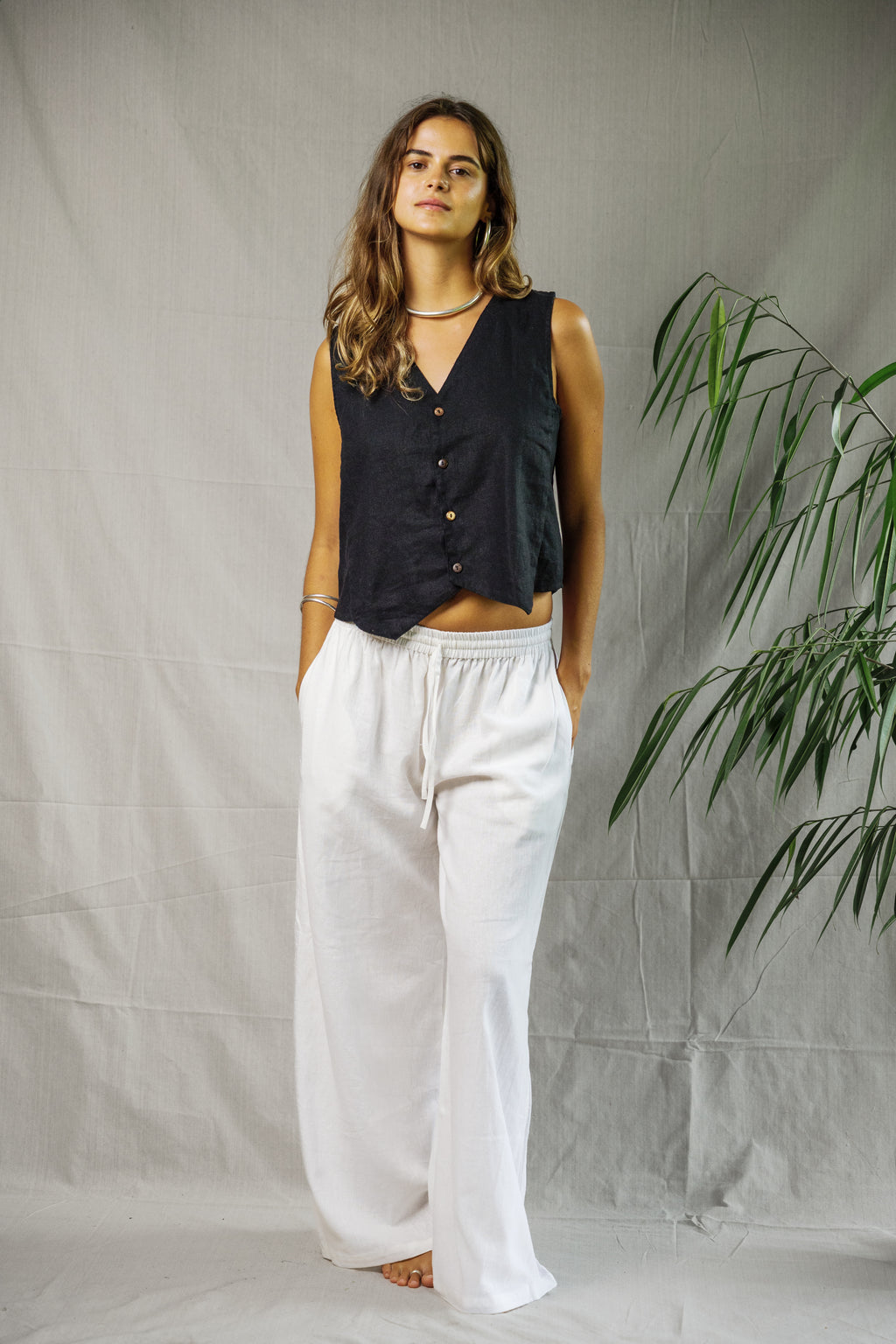 Black sleeveless linen vest with buttons and v-neck paired with loose white linen pants.