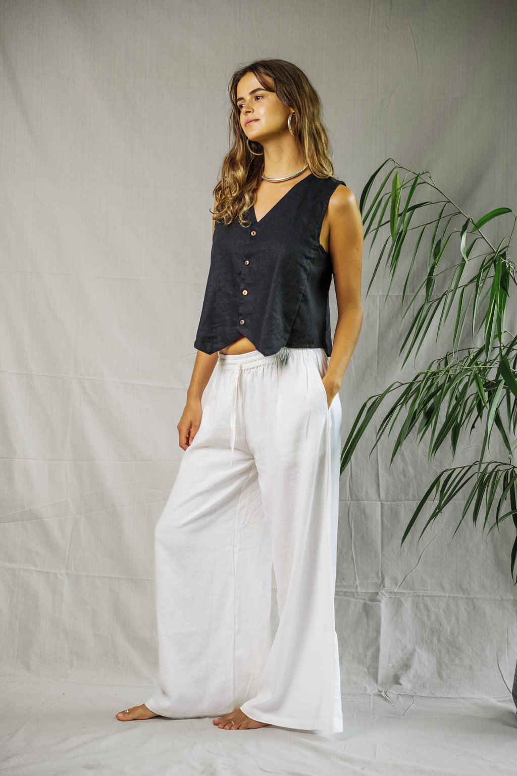 Black sleeveless button-up linen vest with V-neck on model paired with white wide-leg pants.