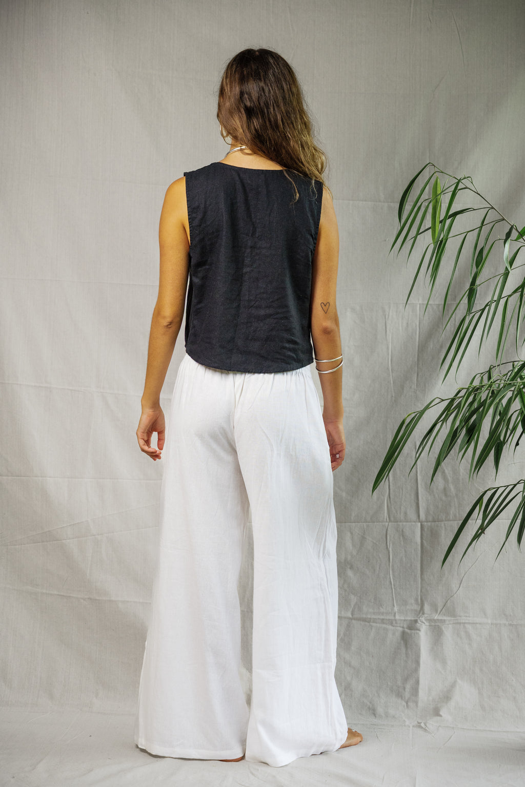 Black sleeveless linen vest with a relaxed fit on a model, paired with white wide-leg pants.