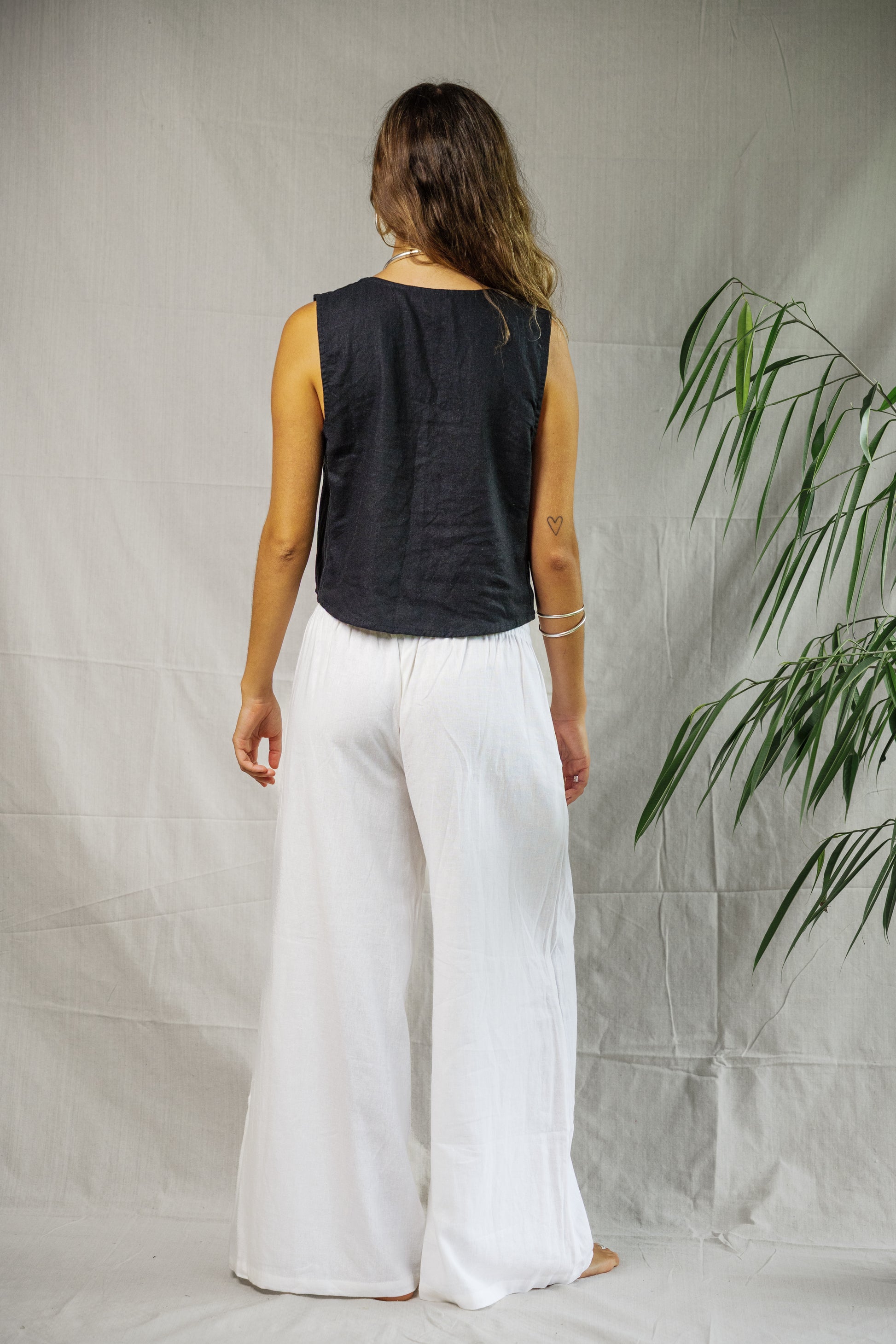 Black sleeveless linen vest with a relaxed fit on a model, paired with white wide-leg pants.