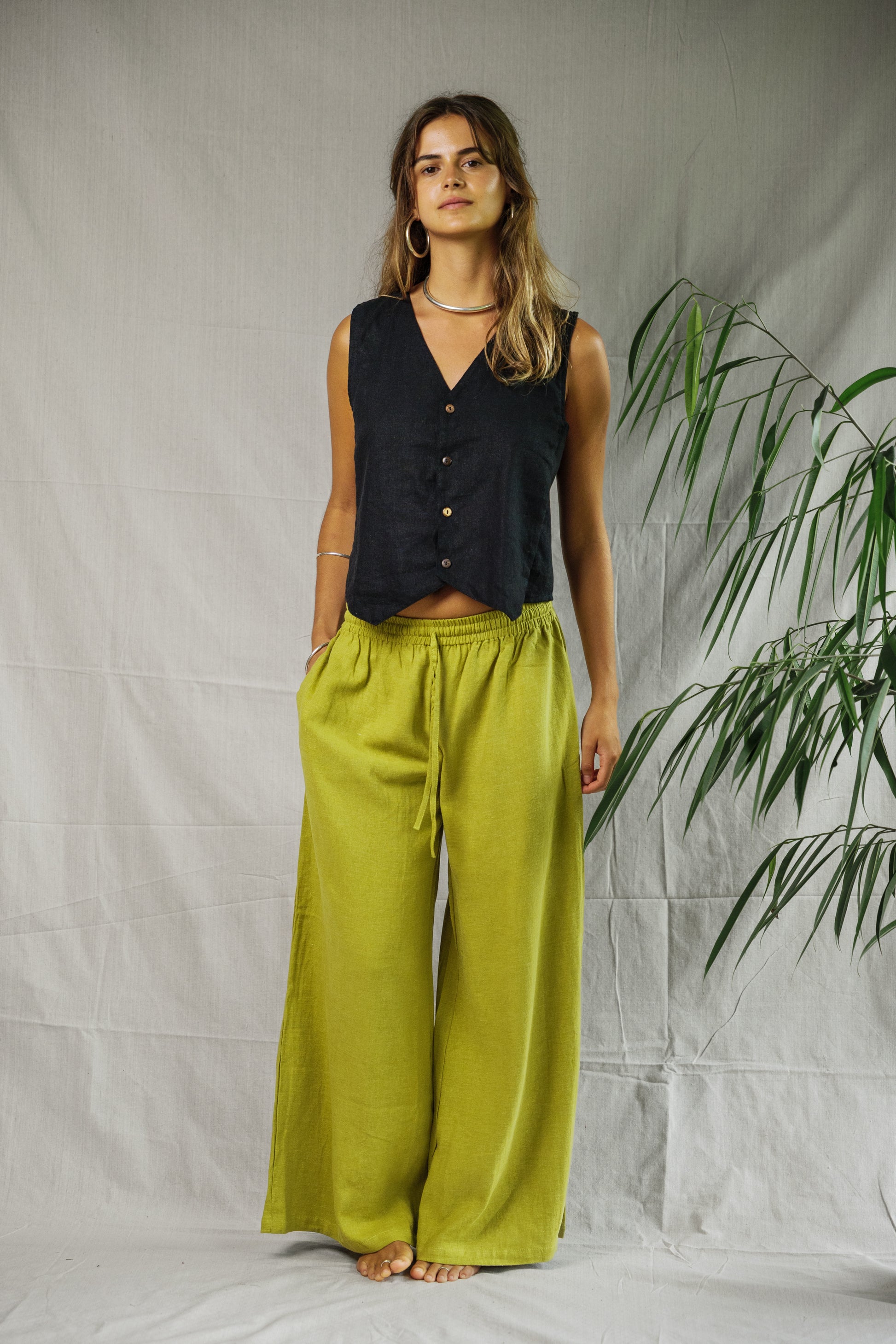 Black sleeveless linen vest with buttons, worn with loose pistachio wide-leg pants.