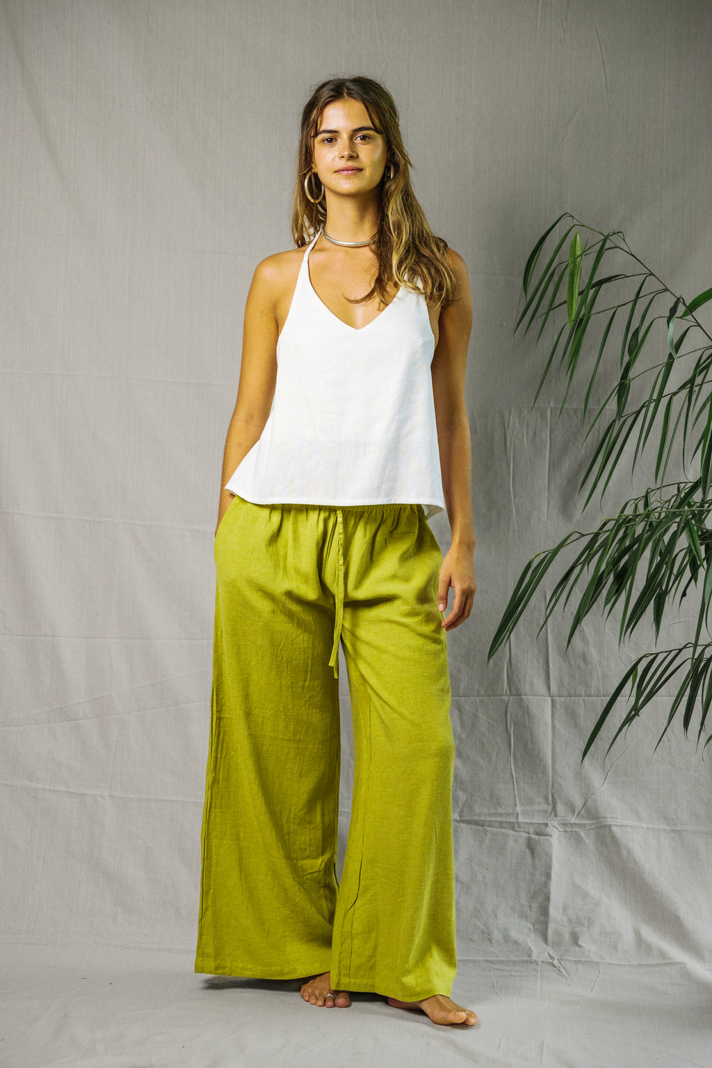 White linen halter top paired with loose lime green wide-leg pants on model against gray backdrop.