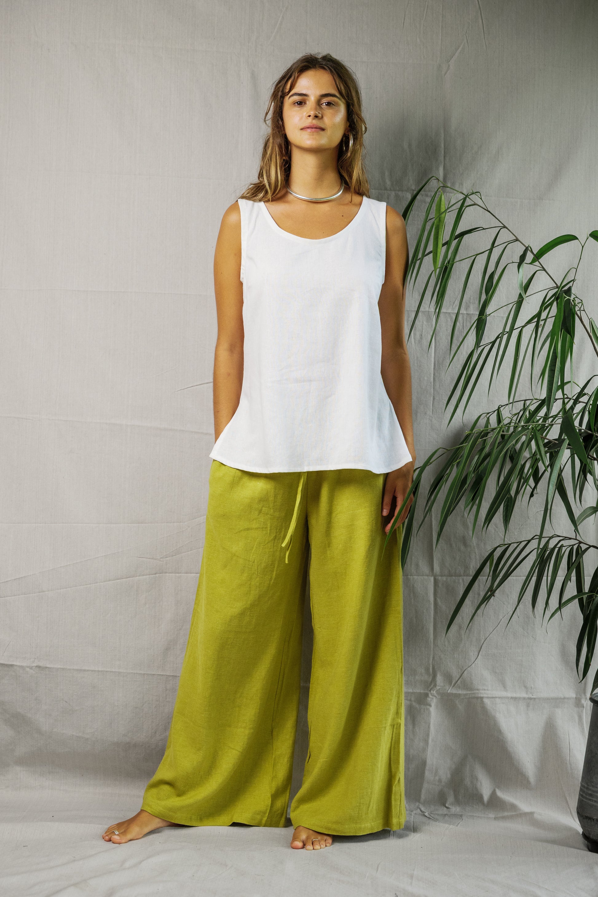 White sleeveless linen singlet with scoop neckline and relaxed fit worn with loose lime green pants.