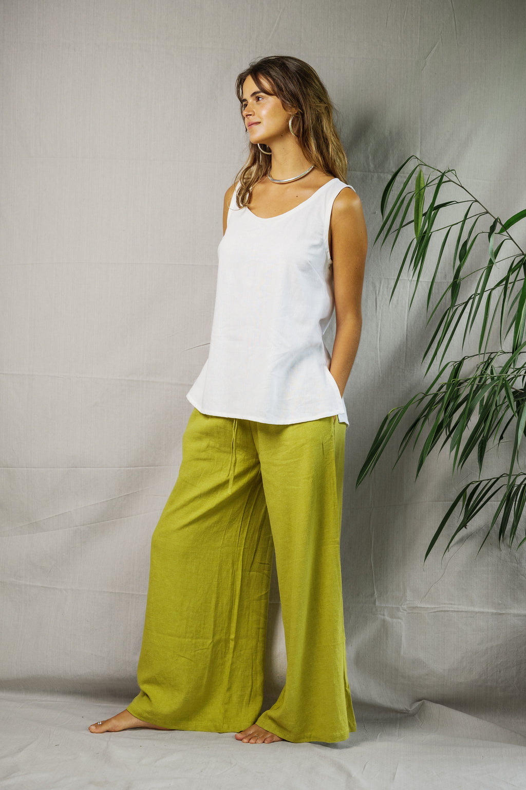 White sleeveless breathable linen singlet paired with loose bright green wide-leg pants on female model.