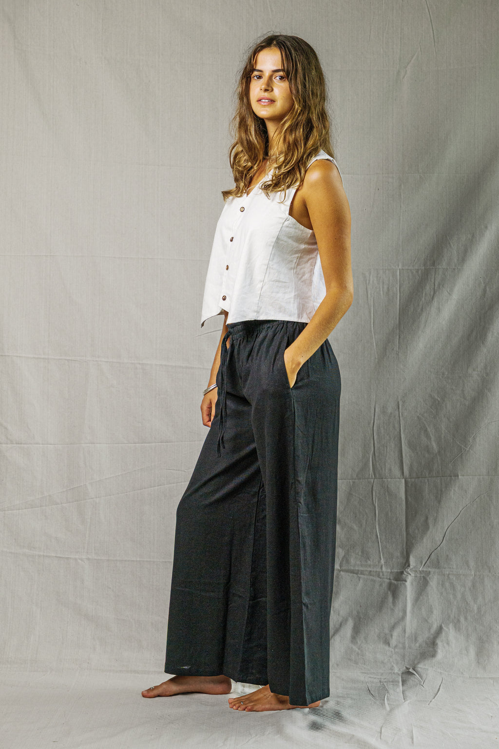 Sleeveless white linen vest with buttons and relaxed fit modeled with black wide-leg pants.
