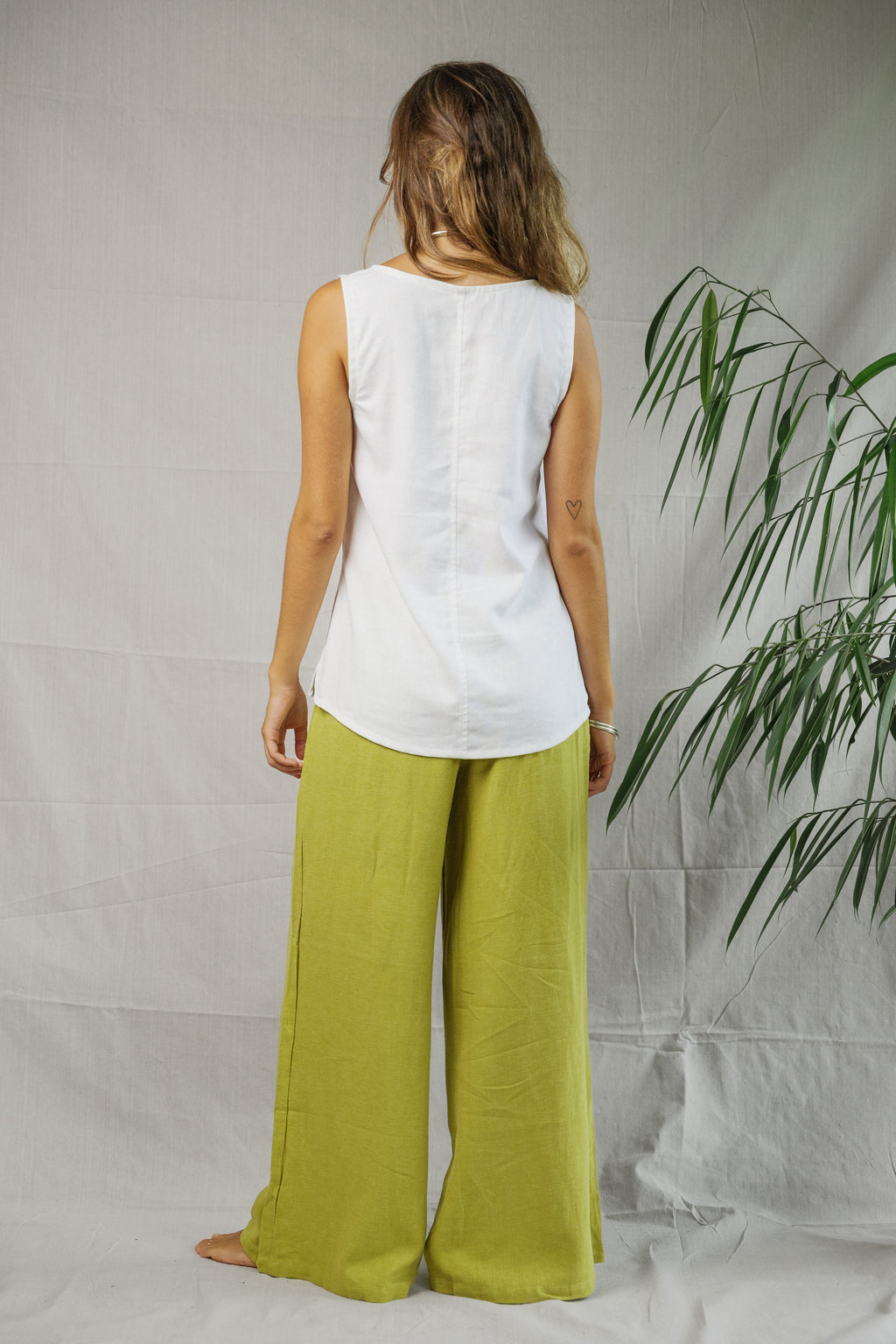 White sleeveless linen singlet with scoop neck and curved hem, worn with loose lime green pants.