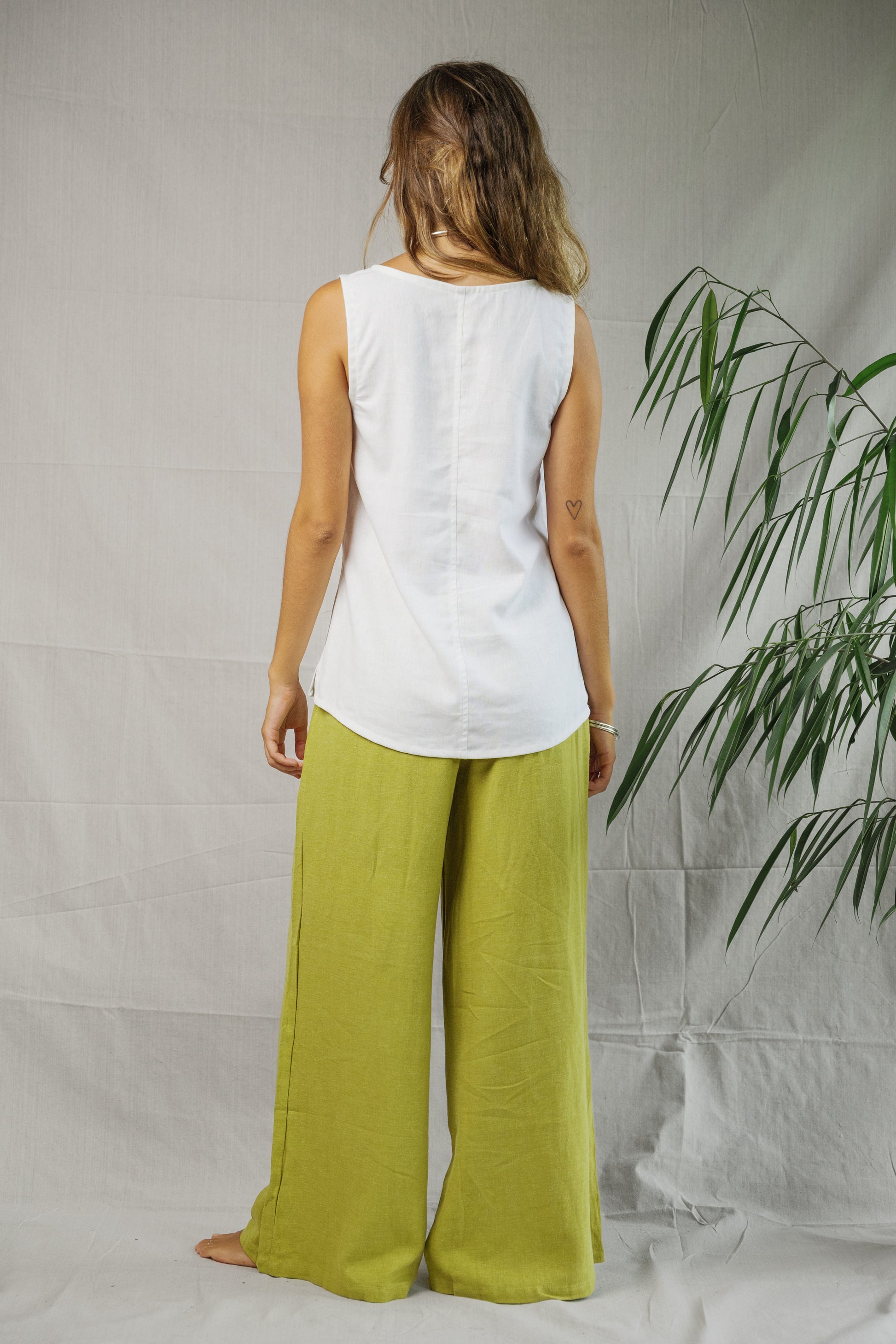 White sleeveless linen singlet with scoop neck and curved hem, worn with loose lime green pants.