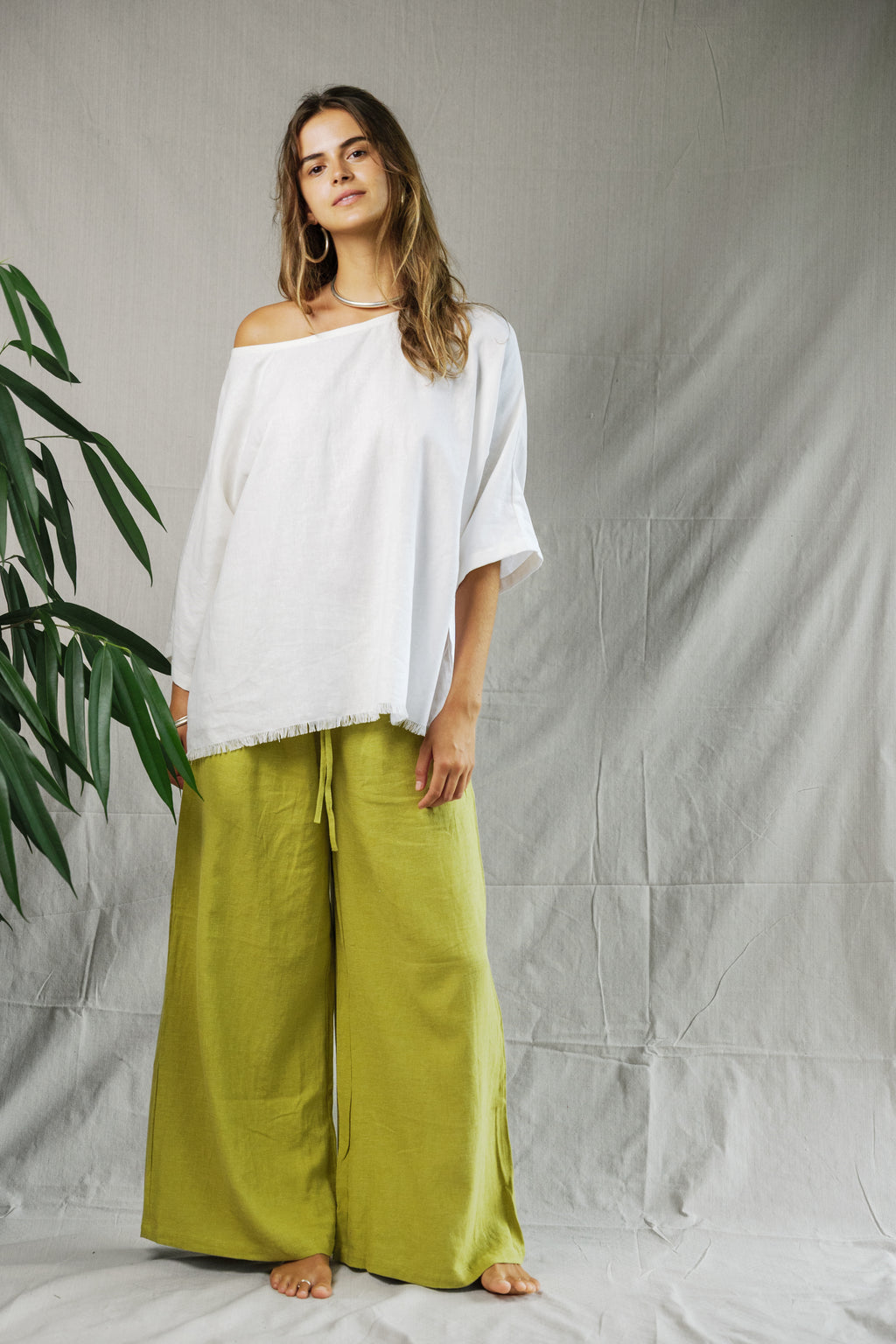 Loose white linen tee with wide sleeves and off-shoulder neckline paired with olive wide-leg pants.