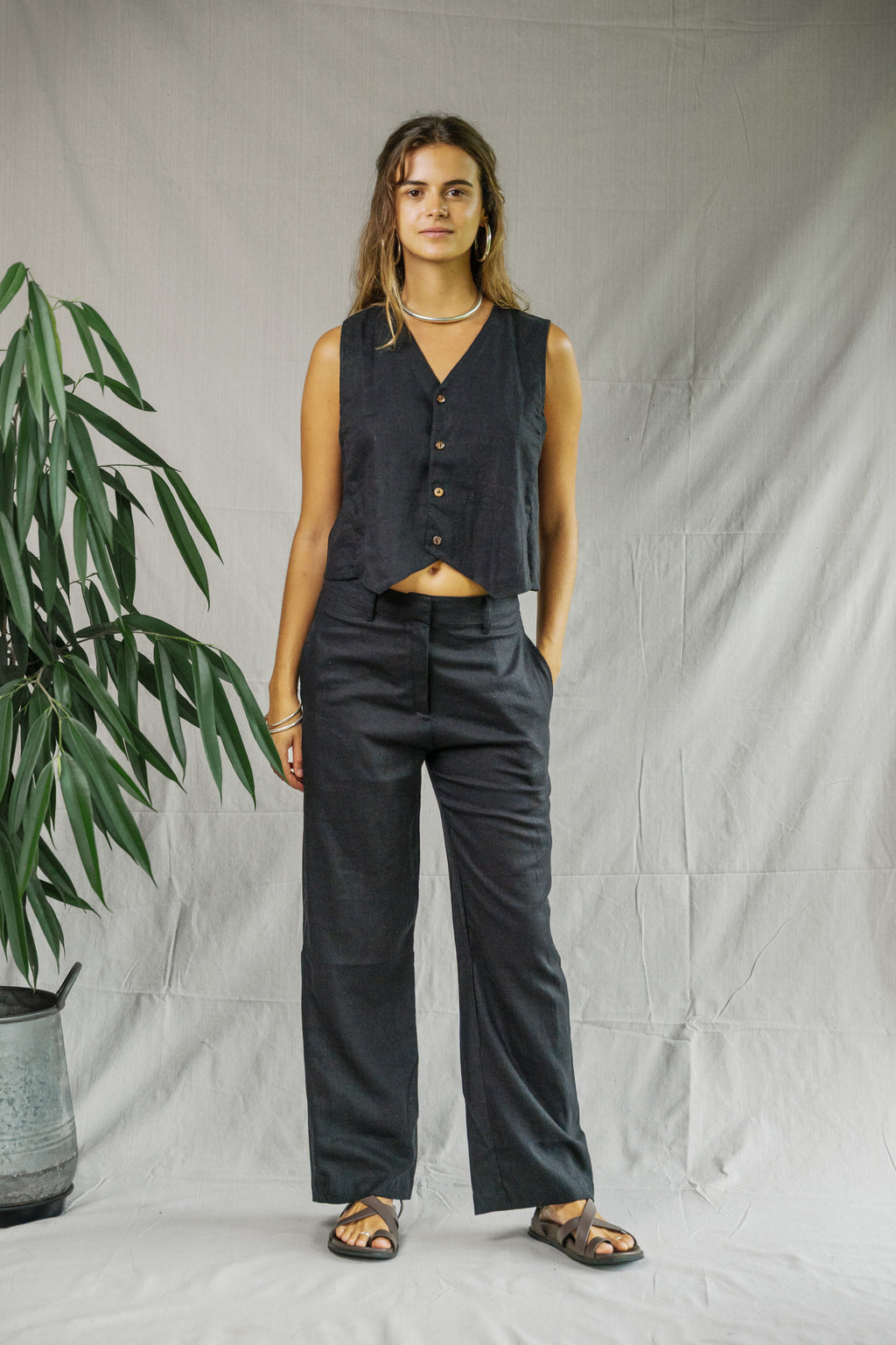 Black sleeveless linen vest with buttons paired with matching wide-leg linen pants and black sandals.