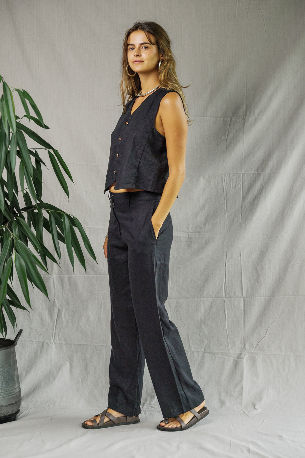 Black sleeveless linen vest with button front and relaxed fit worn with matching pants.