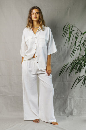 White breathable linen button-up Sol Shirt with three-quarter sleeves and relaxed fit worn with matching wide-leg pants.