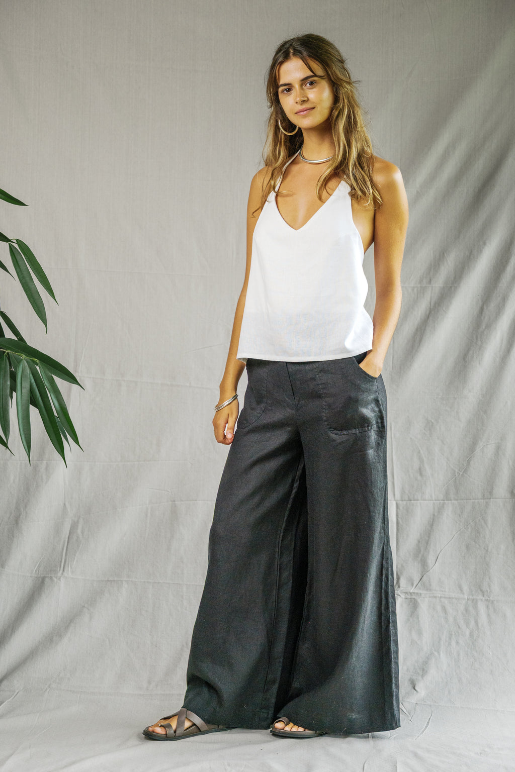 Black wide-leg linen pants with high waist and side pockets worn with white sleeveless top.