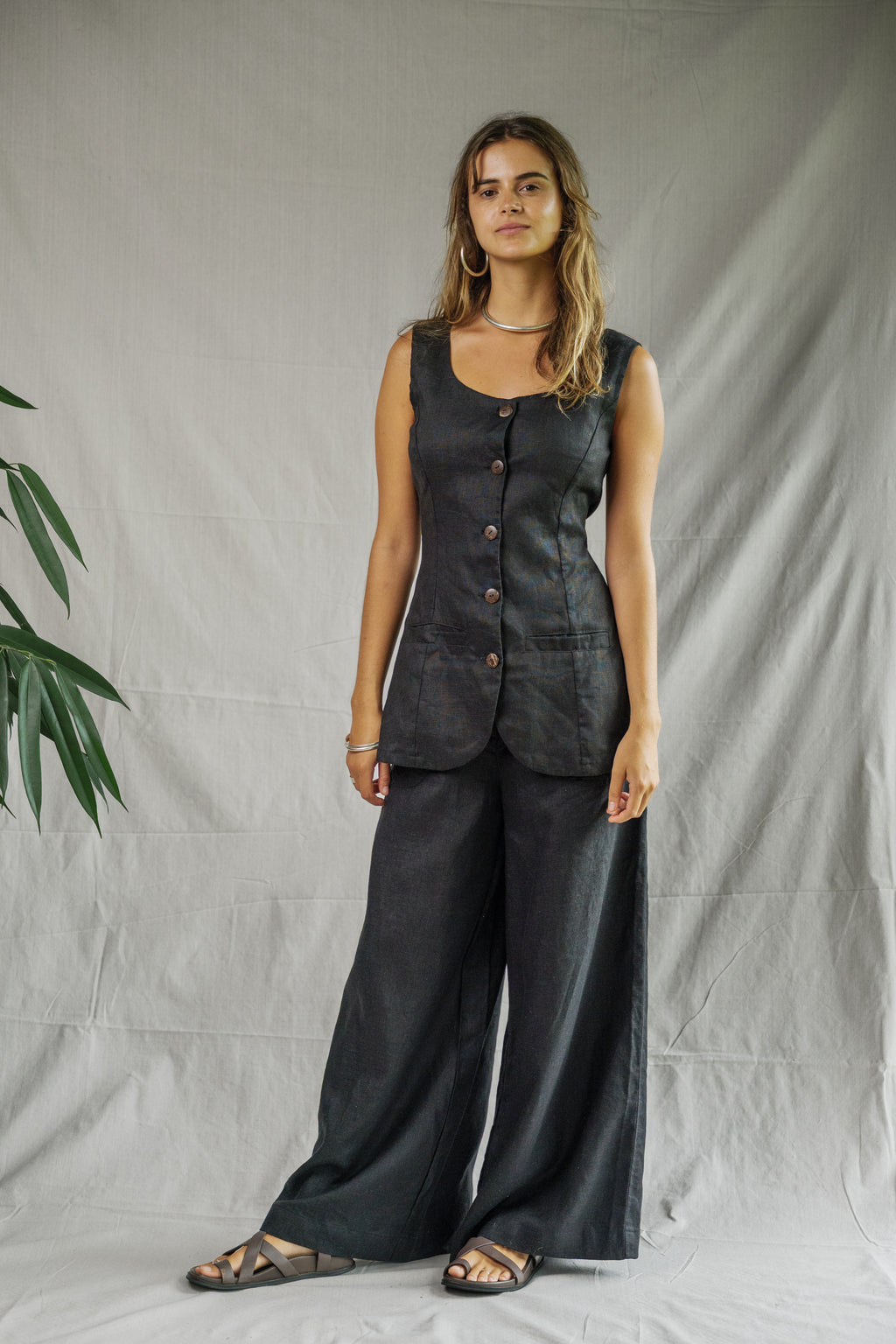 Black sleeveless linen vest with button front and square neckline worn with wide-leg pants.