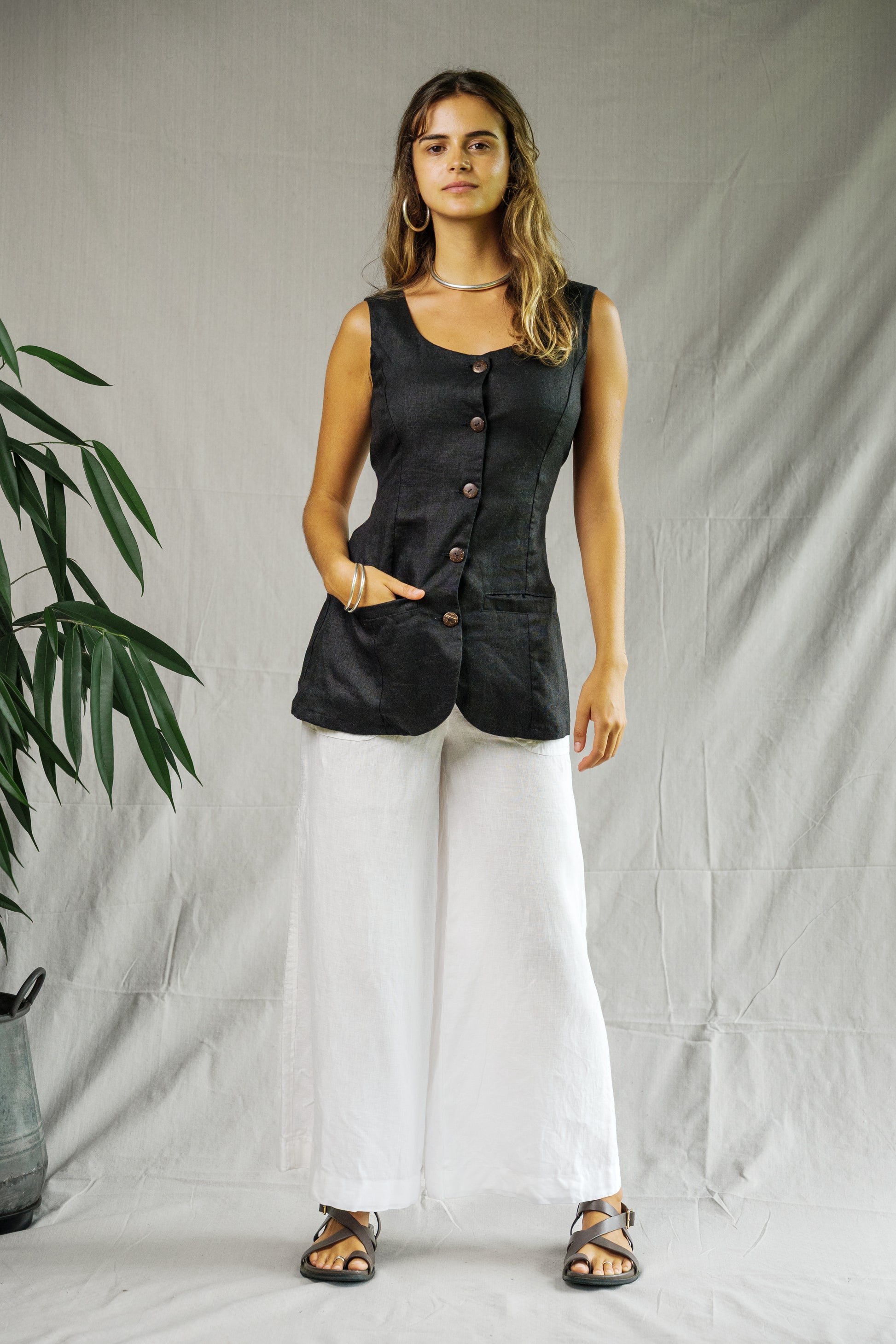 Black sleeveless button-front top with square neckline paired with wide-leg white linen pants.