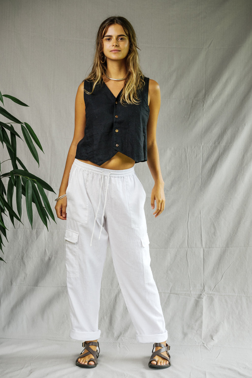 White linen cargo pants with multiple pockets, relaxed fit, worn with black sleeveless button-up top and sandals.