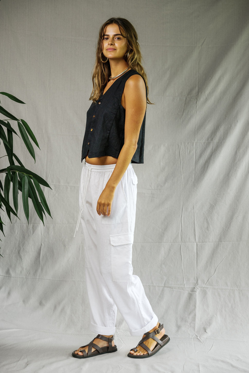 Black sleeveless linen vest with button front, worn with white cargo pants and sandals.