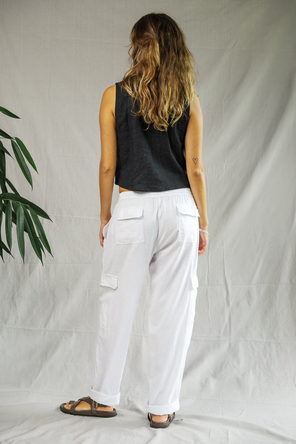 White linen cargo pants with side pockets, loose fit, worn with black sleeveless top and sandals.
