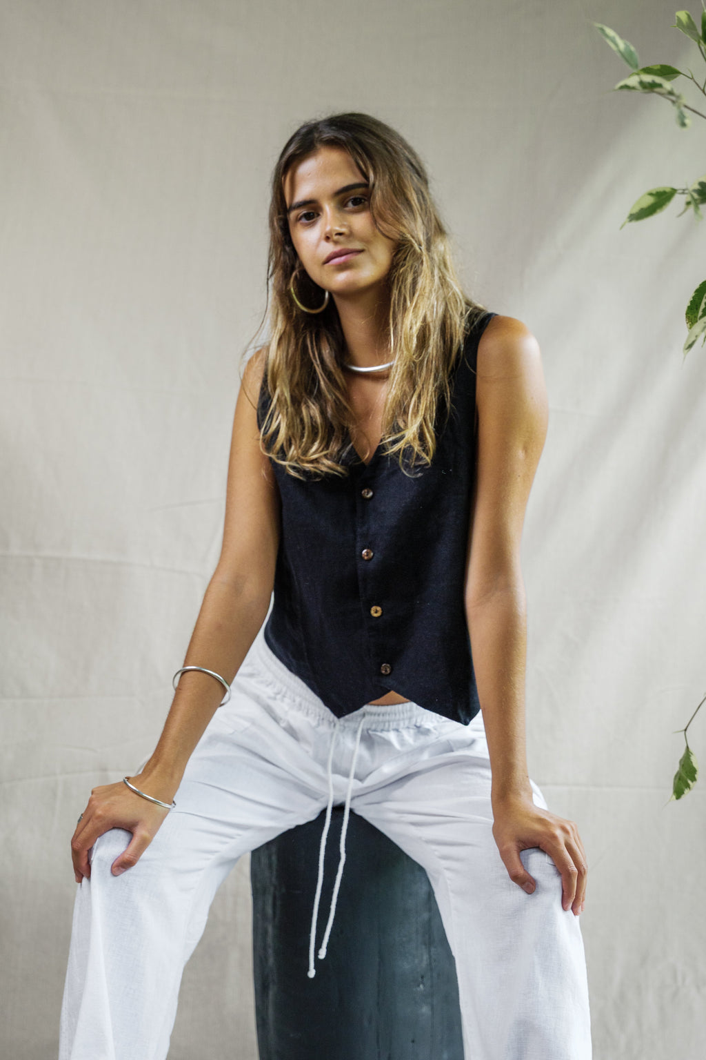Black sleeveless linen vest with button front and V-neck, paired with white drawstring pants.