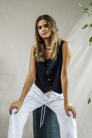 Black sleeveless linen vest with button front and V-neck, paired with white drawstring pants.