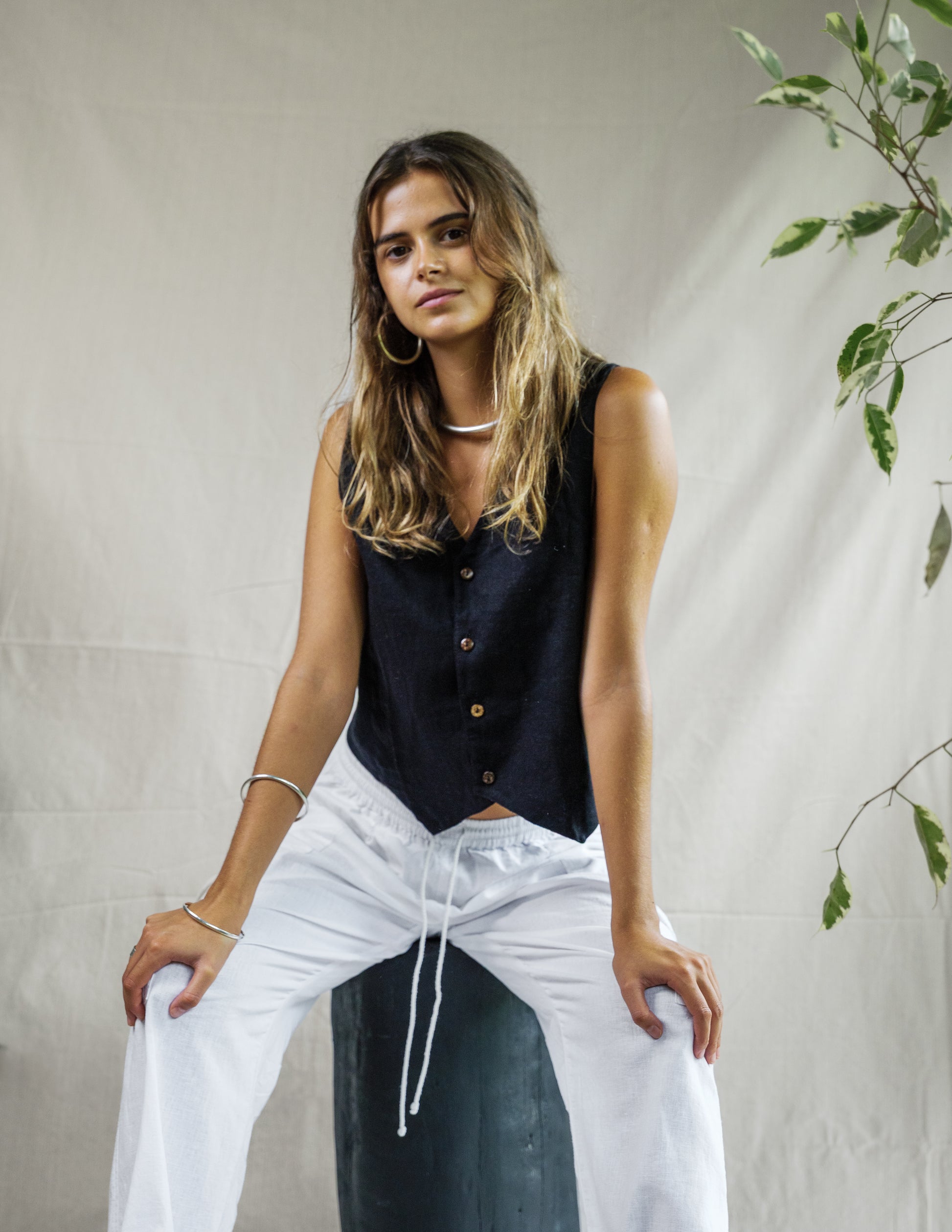 Woman wearing black sleeveless linen vest paired with white breathable cargo pants with drawstring waist.