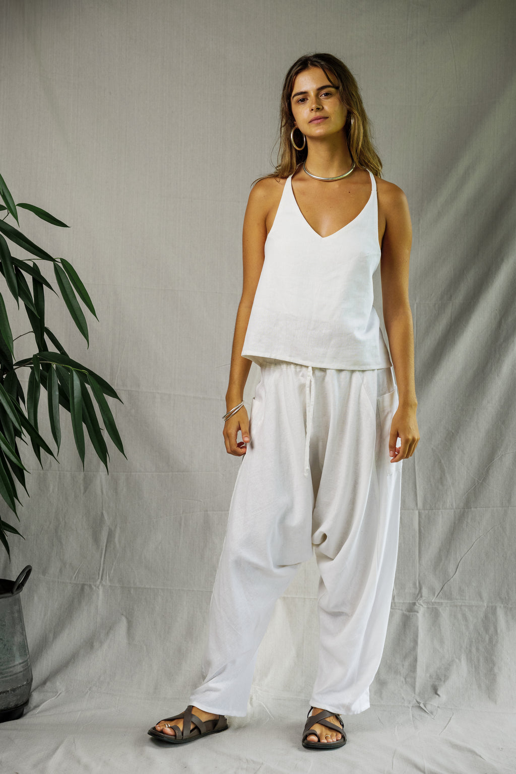 White linen loose-fit pants with elastic waist and side pockets, styled with a white sleeveless top and black sandals.