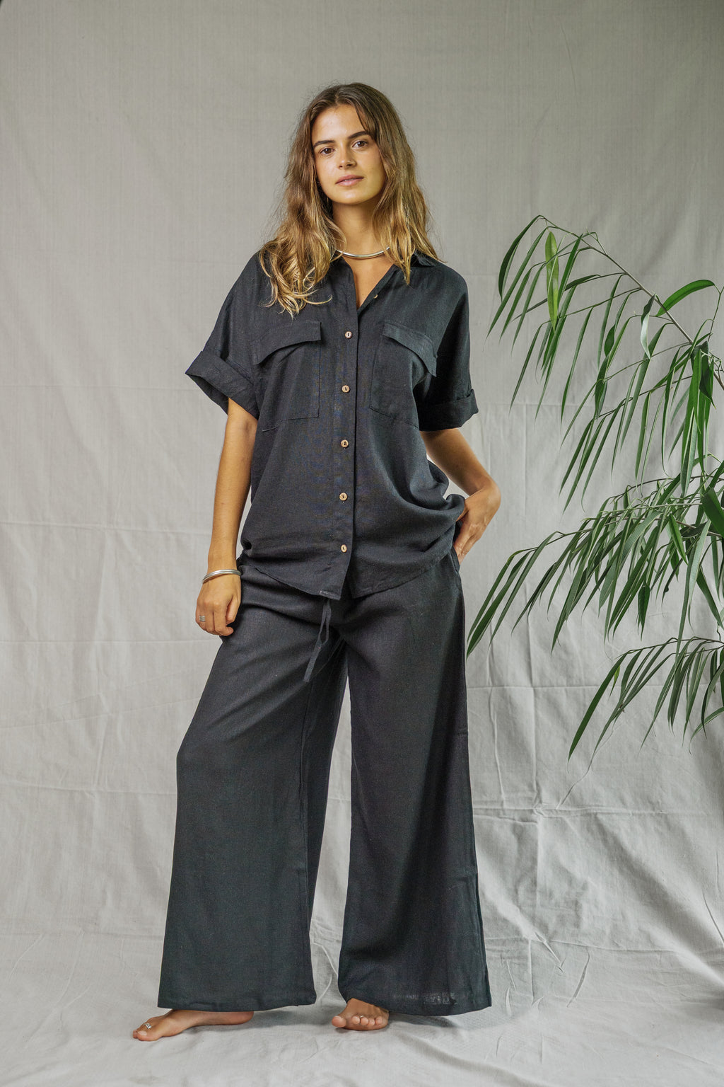 Black linen wide-leg pants with high waist and side pockets worn with matching button-up short-sleeve shirt.
