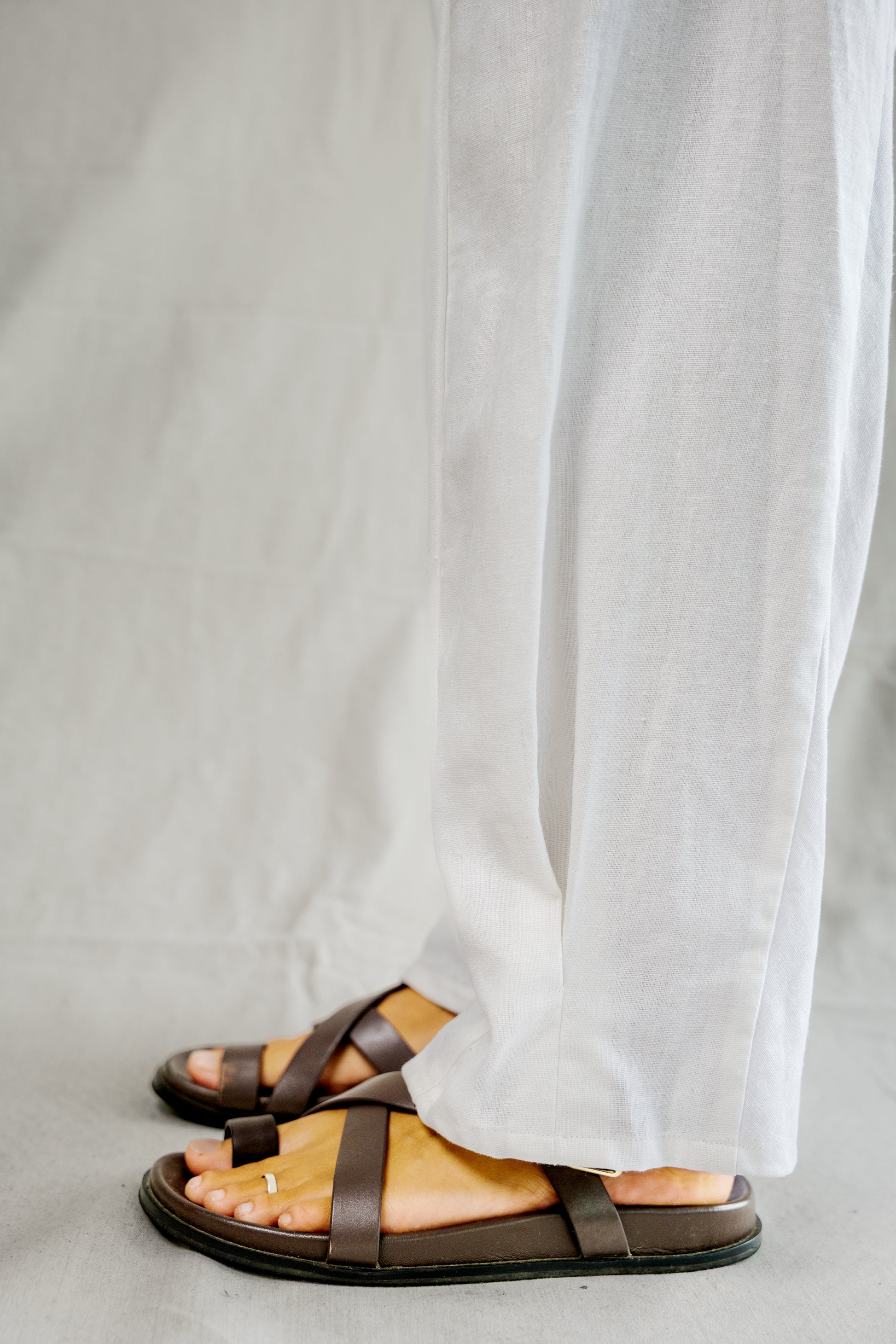 White breathable linen pants with wide legs paired with brown leather sandals.