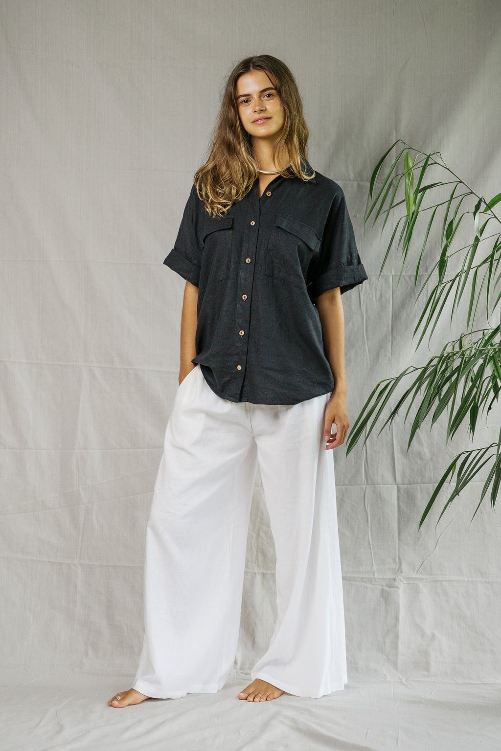 Black short-sleeve linen shirt with brown buttons styled with white wide-leg pants.
