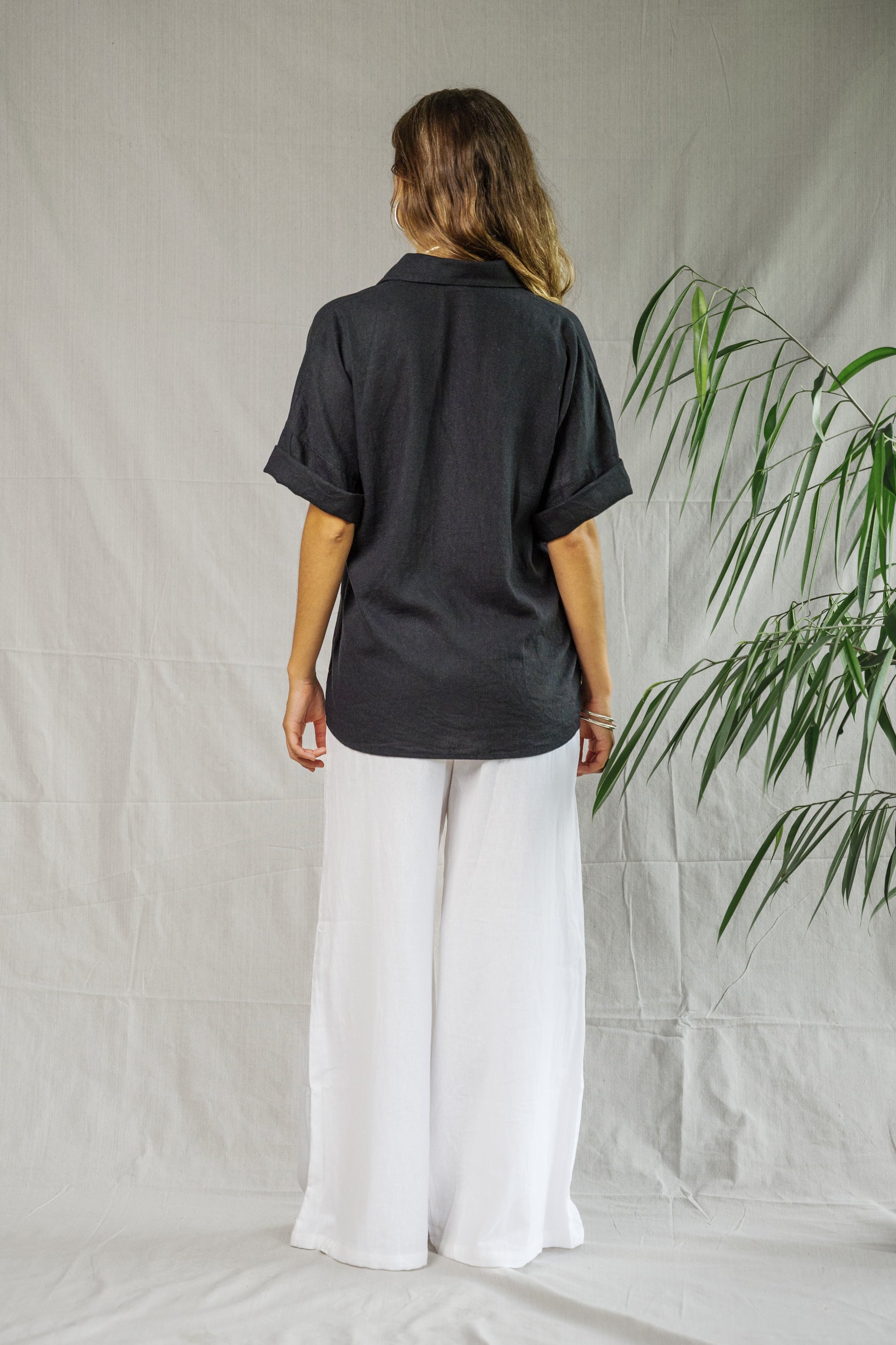 Black short-sleeve breathable linen shirt with relaxed fit on model standing against neutral backdrop.