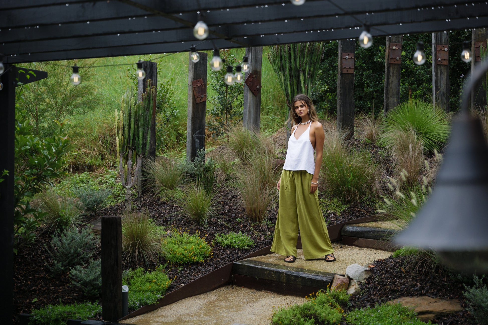 White sleeveless linen halter top with relaxed fit worn with olive green wide-leg pants outdoors.