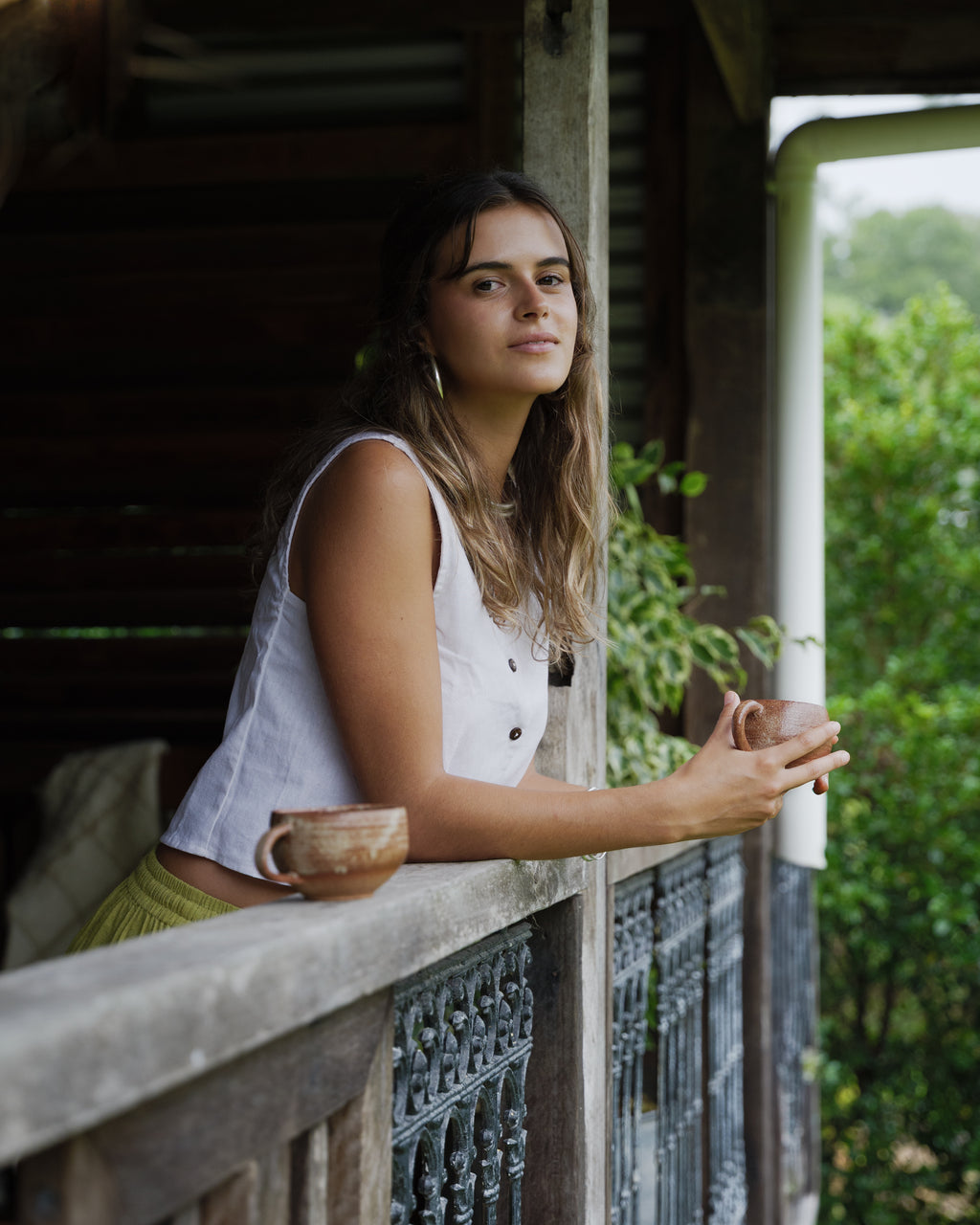 Sleeveless white linen vest with button front and relaxed fit worn outdoors.