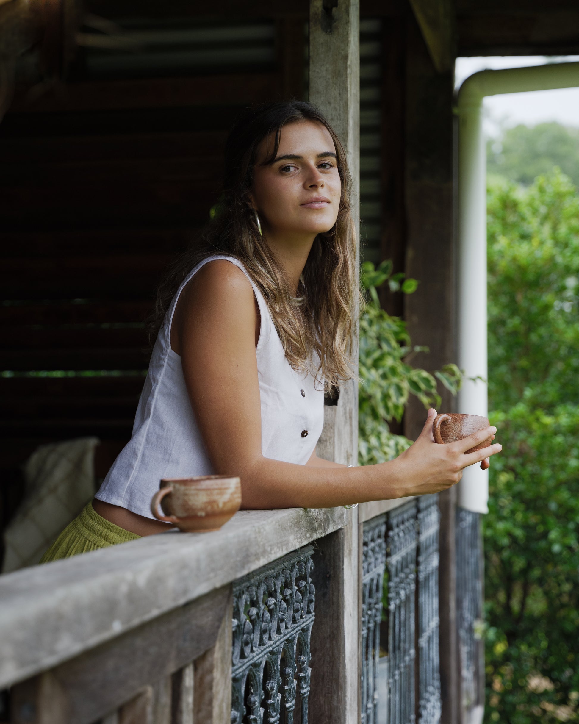Sleeveless white linen vest with button front and relaxed fit worn outdoors.