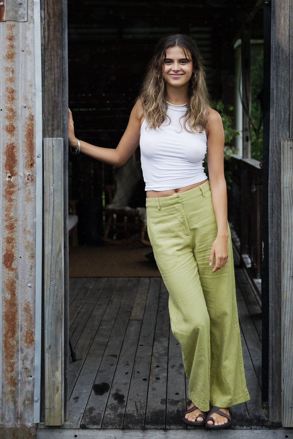 Woman wearing pistachio green linen wide-leg pants with high waist and belt loops paired with a white sleeveless ribbed top.