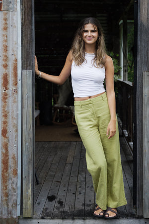 Woman wearing pistachio green linen wide-leg pants with high waist and belt loops paired with a white sleeveless ribbed top.