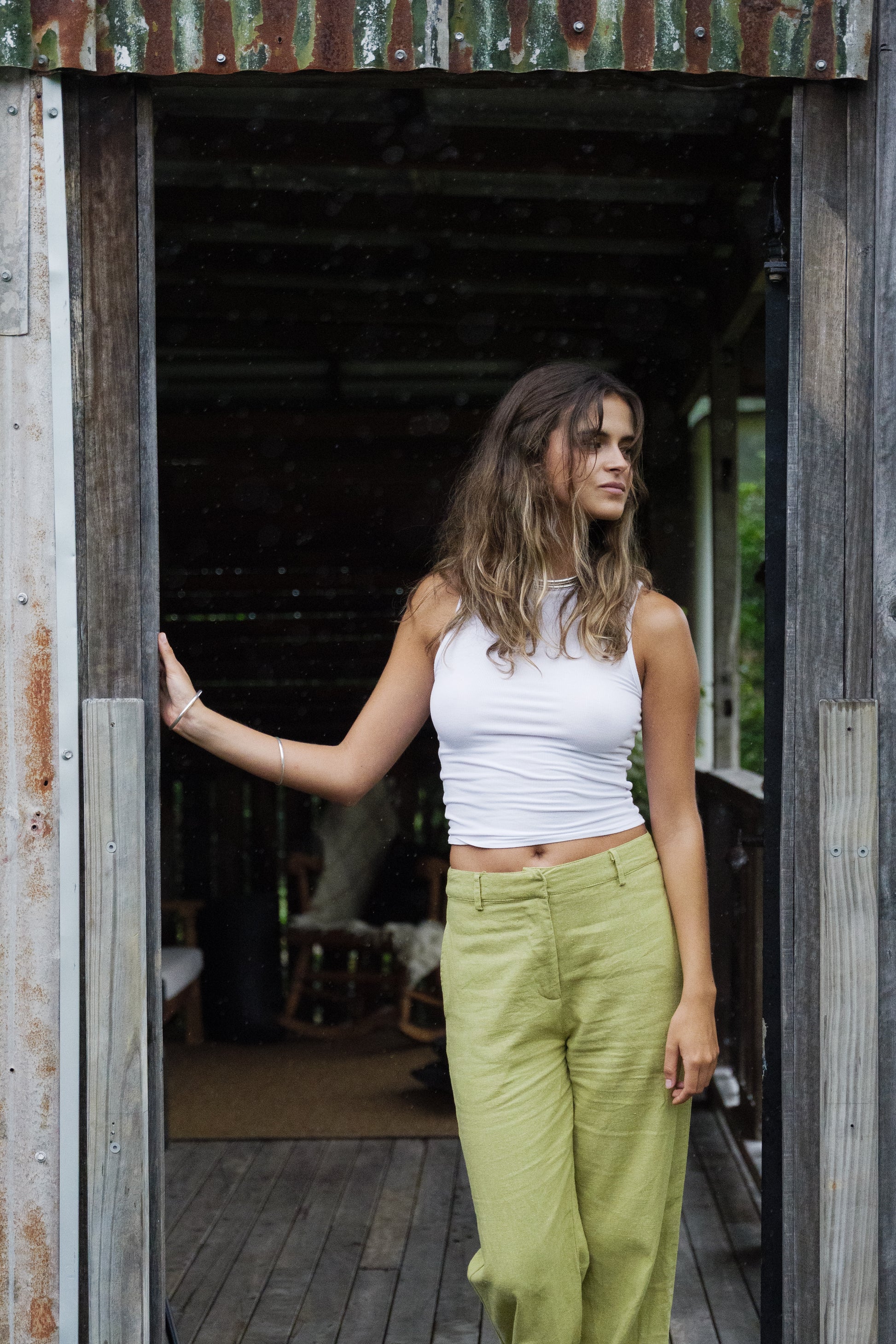 Woman wearing pistachio green breathable linen pants with a high waist and relaxed fit paired with a white sleeveless top.