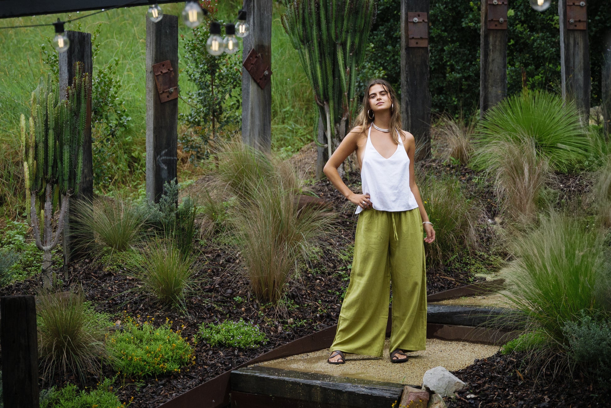 White linen halter top paired with wide-leg olive green pants in outdoor garden setting.