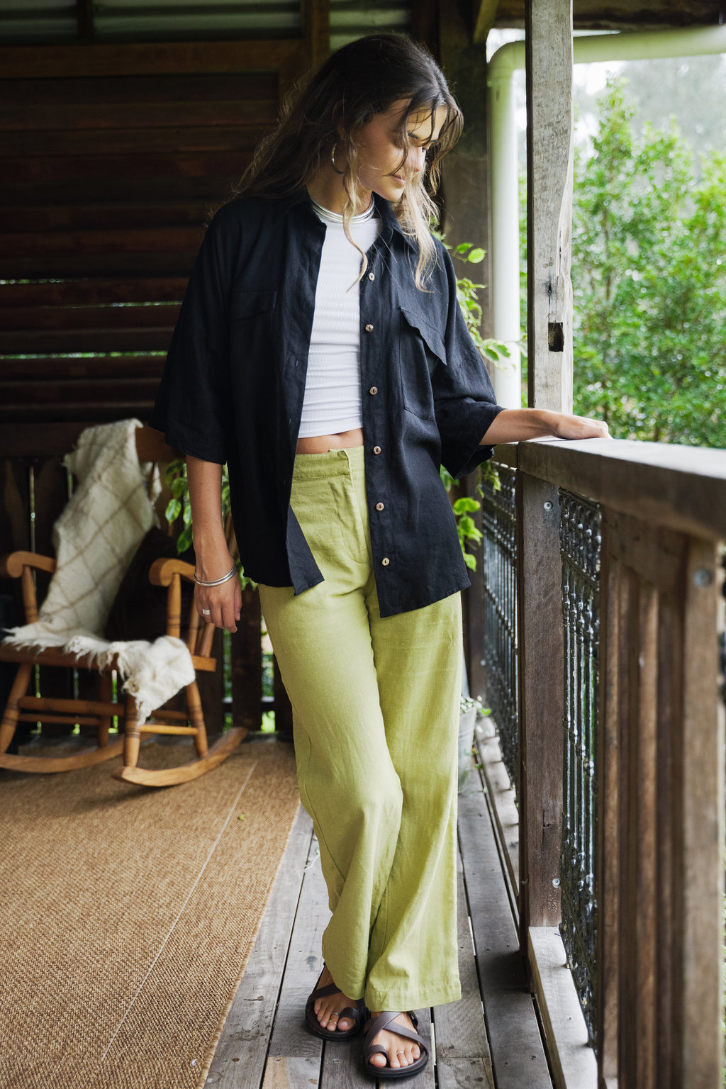 Black linen Sol Shirt with short sleeves worn open over white top, paired with pistachio wide-leg pants.