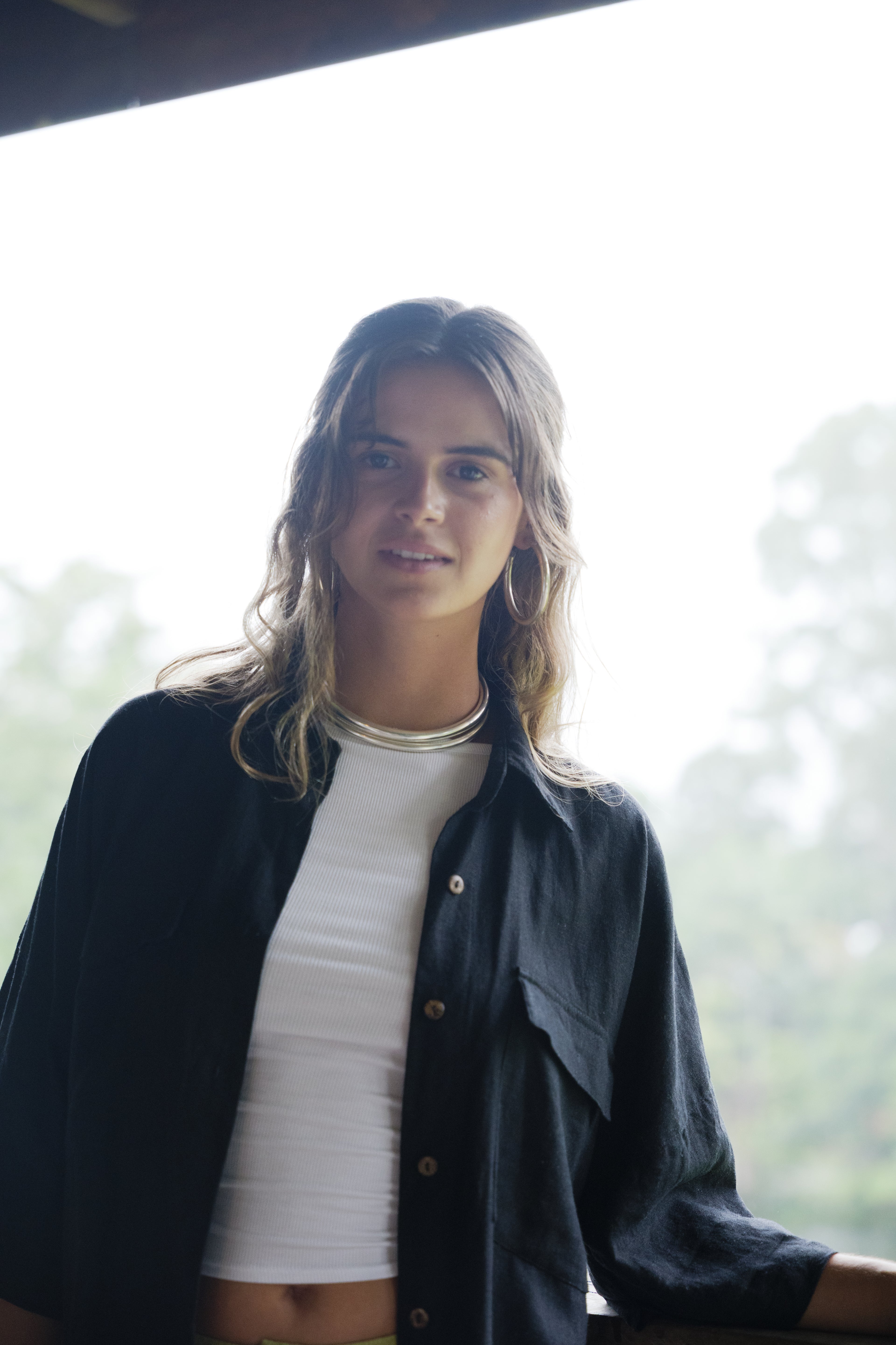 Black breathable linen Sol Shirt with button front and chest pocket worn open over white ribbed crop top.