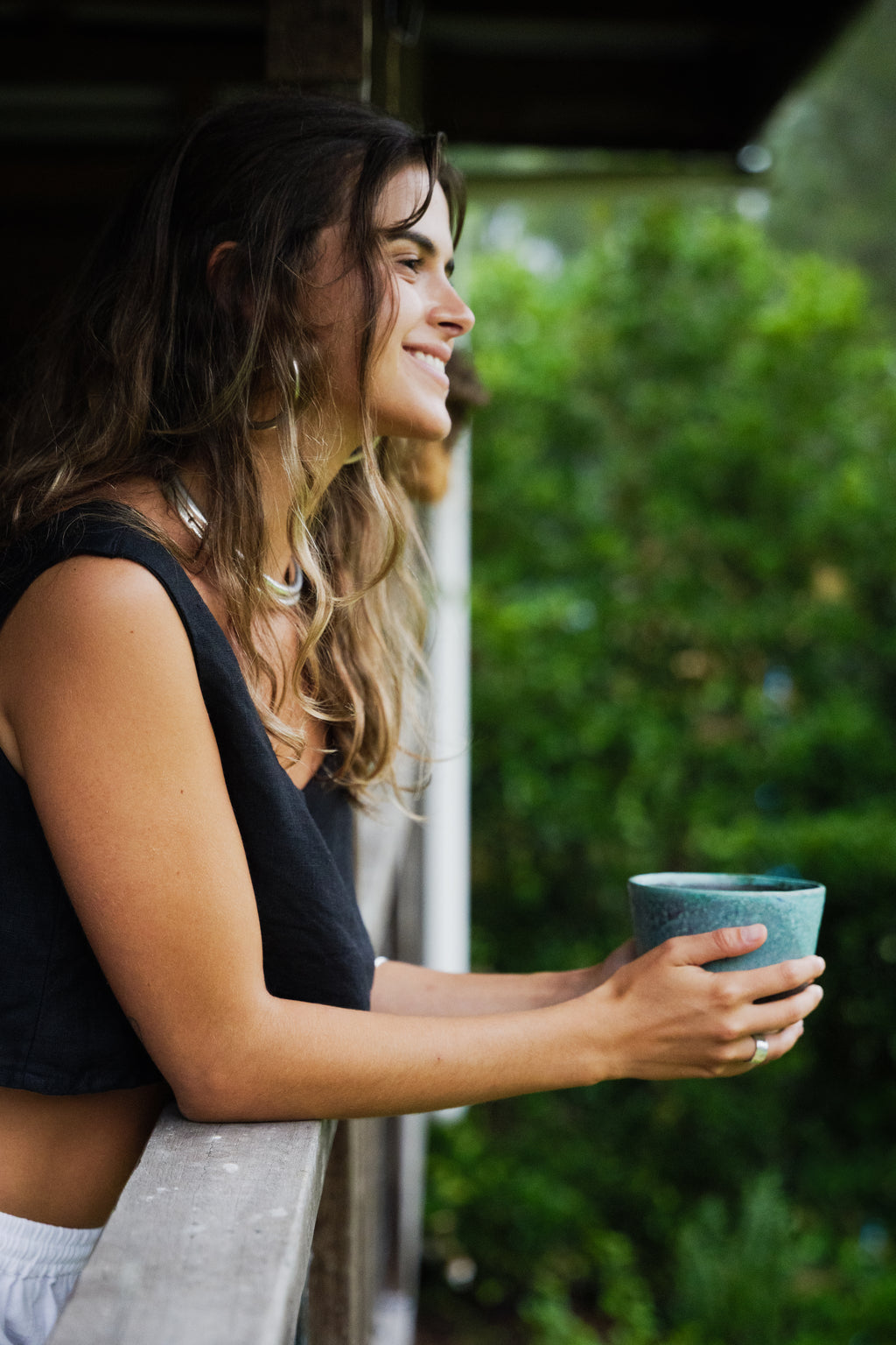 Black sleeveless linen crop top worn by woman holding a blue ceramic cup outdoors.