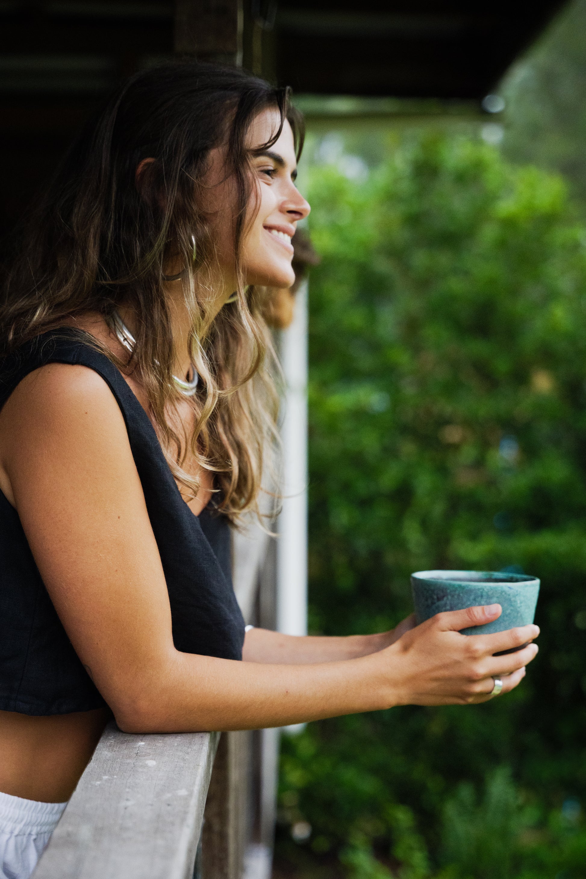 Black sleeveless linen crop top worn by woman holding a blue ceramic cup outdoors.