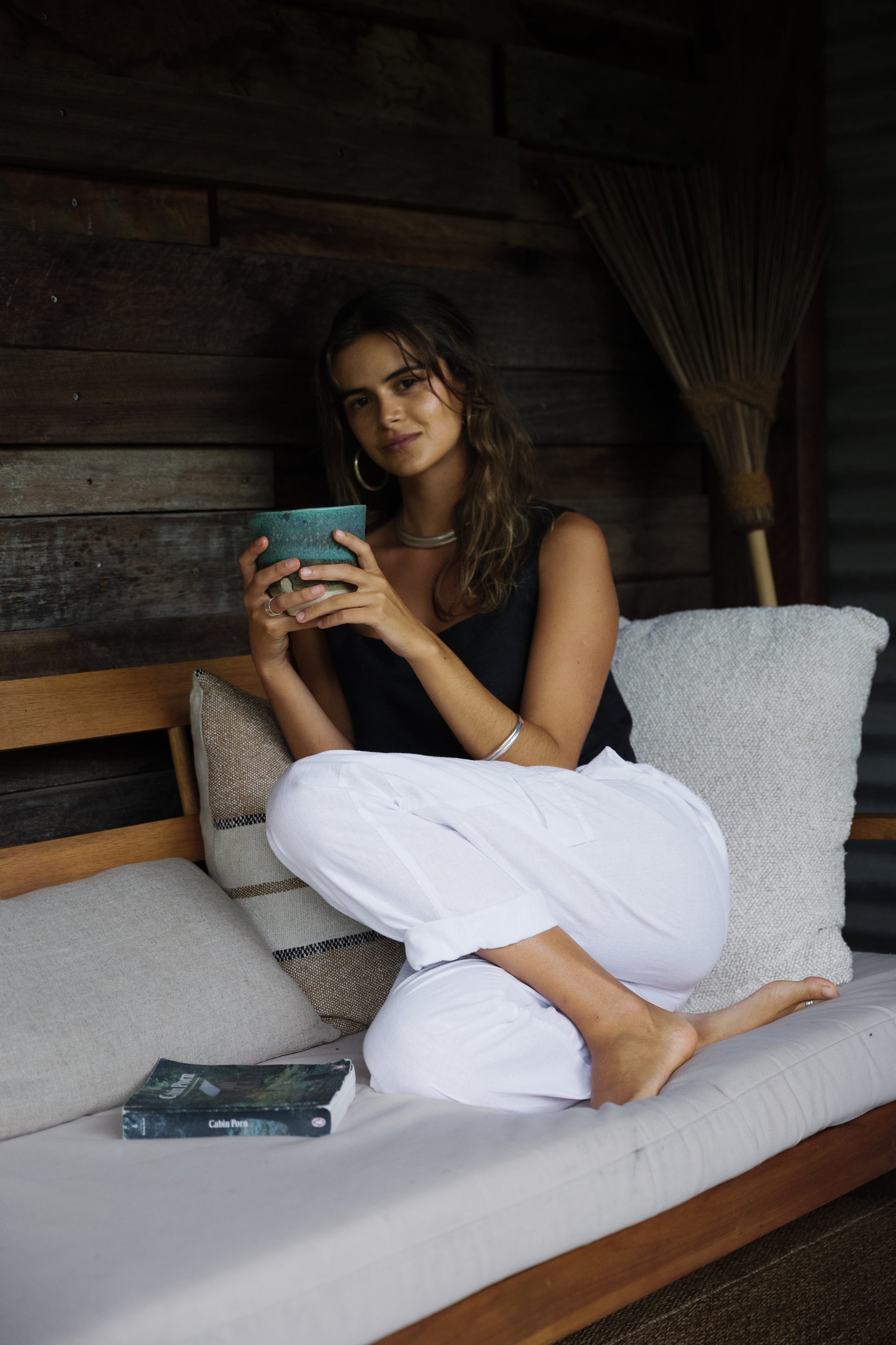 Black sleeveless linen crop top worn by seated woman with long hair on wooden bench with white cushions.