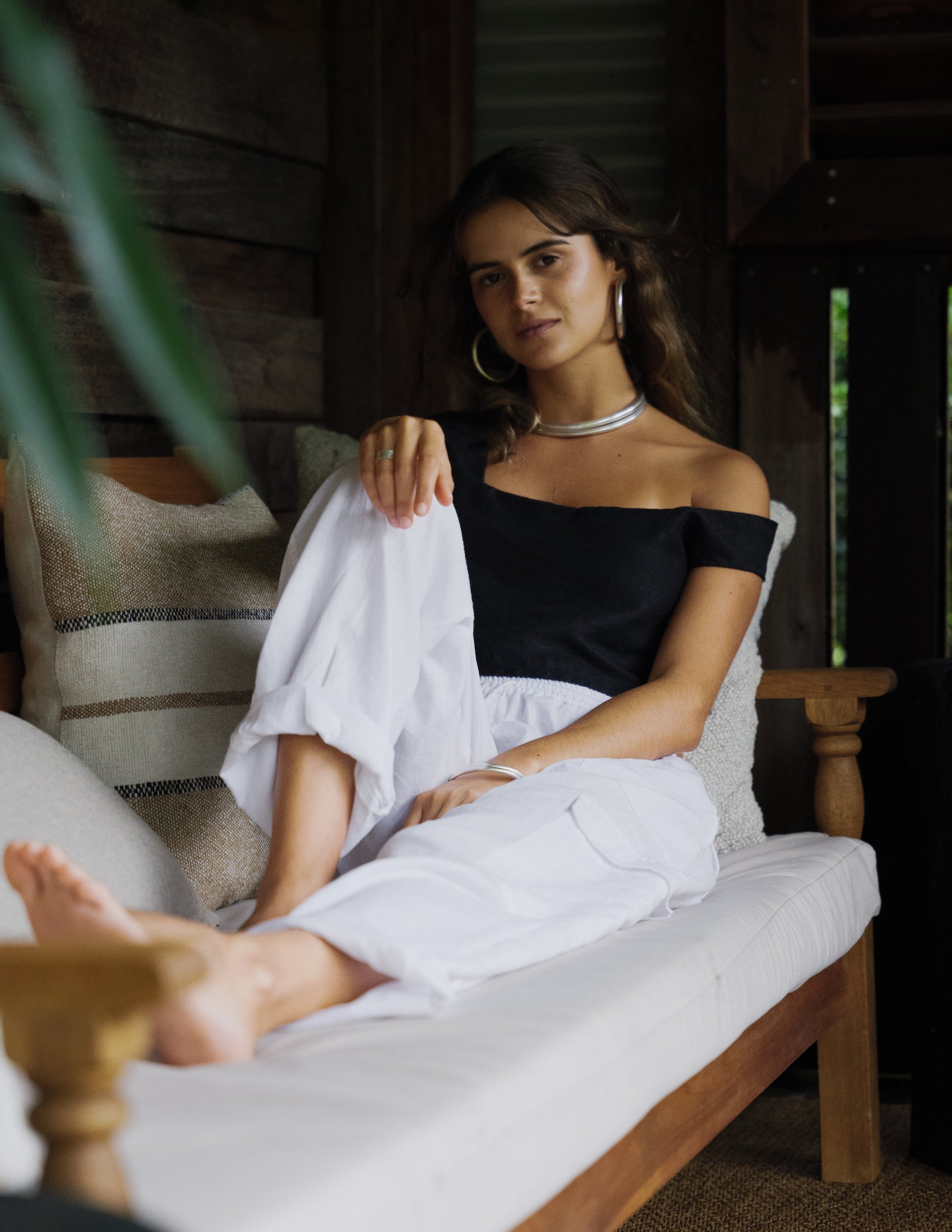 Black off-shoulder crop top paired with white linen cargo pants on seated model.