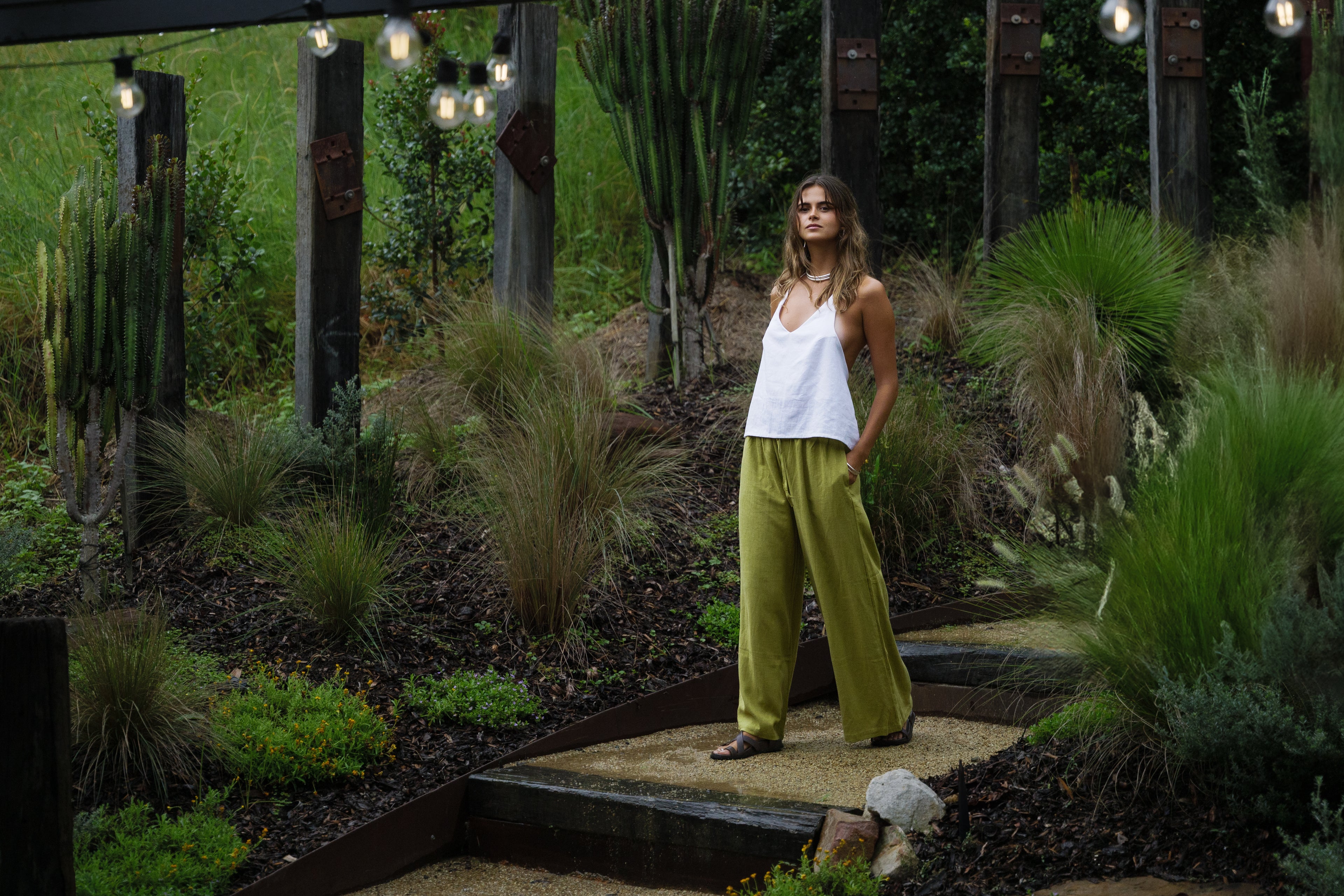 White linen halter top paired with olive green wide-leg pants in a garden setting.