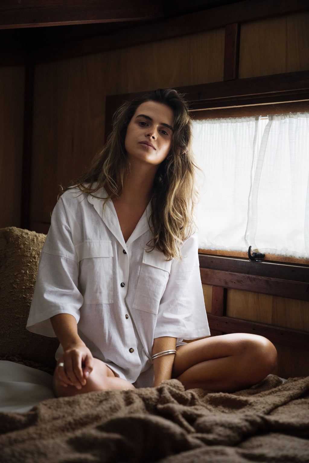 White linen Sol Shirt with button front and relaxed fit worn by seated woman indoors.