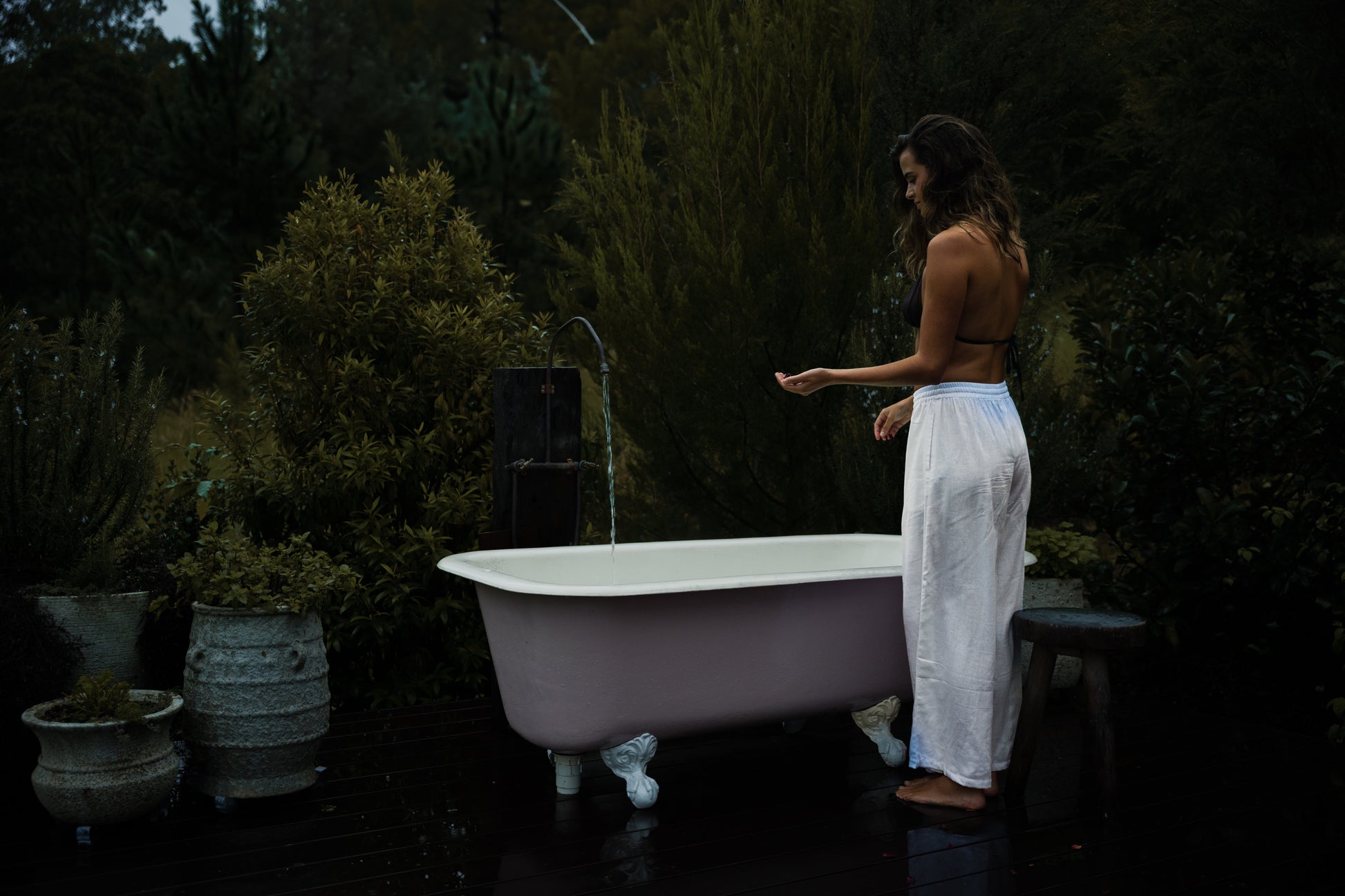 White linen Sol Pants with relaxed fit and cropped length worn by a woman standing beside a freestanding bathtub outdoors.