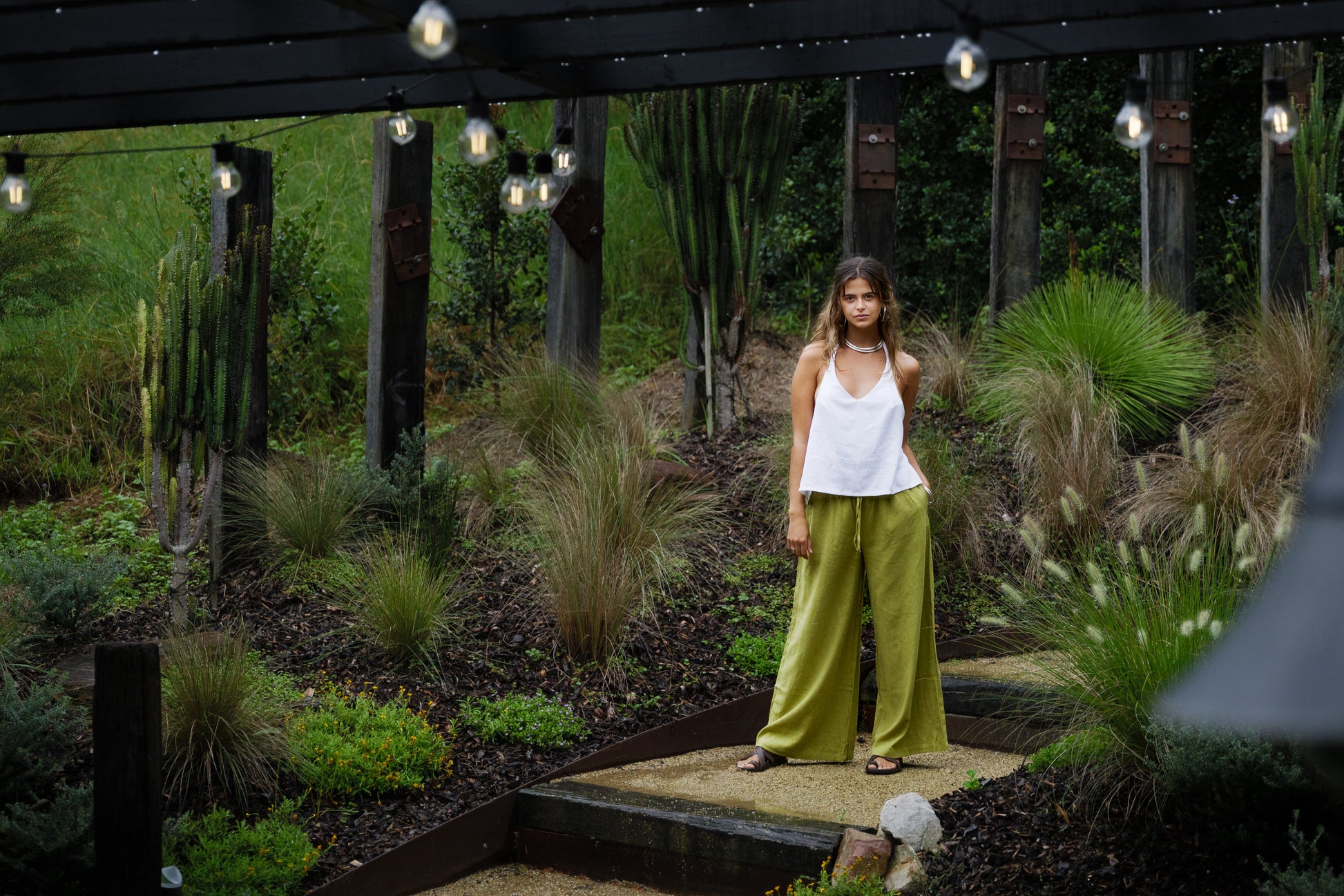 Woman wearing breathable olive green wide-leg linen pants with a white sleeveless top outdoors.