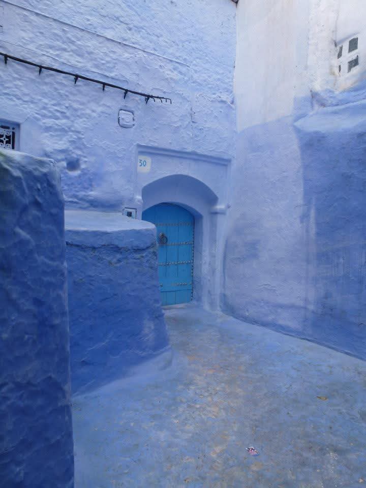 Blue alleyway with white walls and a blue door in Chefchaouen, Morocco.