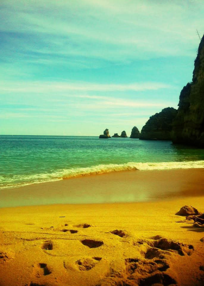 Beach with footprints, turquoise water, and cliffs under a blue sky.